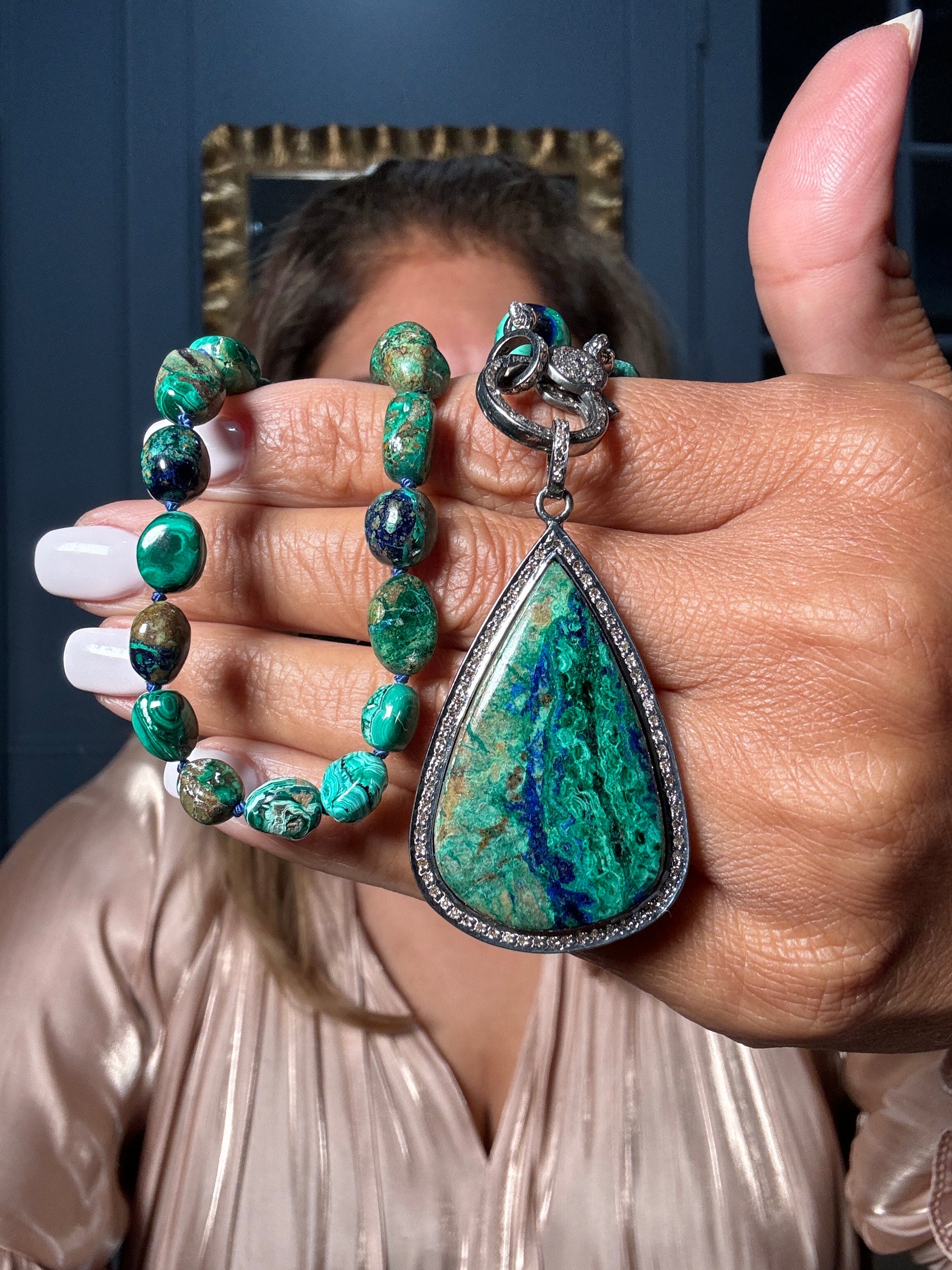 Hand holding an 18-inch azurite-malachite beaded necklace with teardrop-shaped azurite-malachite pendant in sterling silver diamond-accented setting, displaying vibrant green and blue stones.