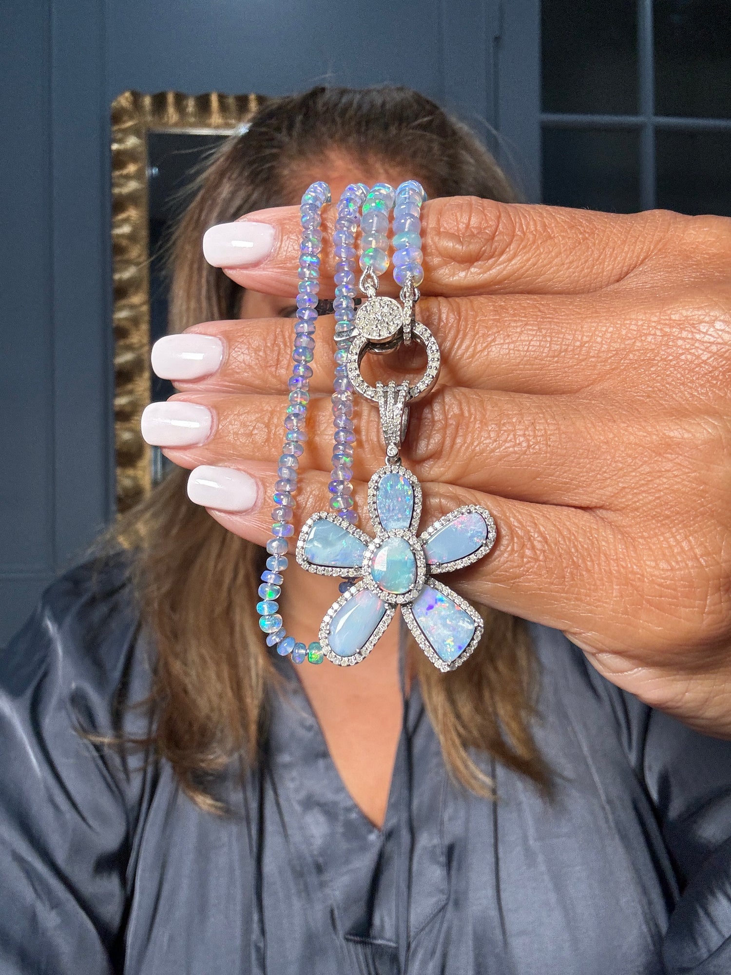 Hand holding an 18-inch Ethiopian opal beaded necklace with large opal flower pendant featuring cool blue and purple tones, sterling silver diamond clasp visible