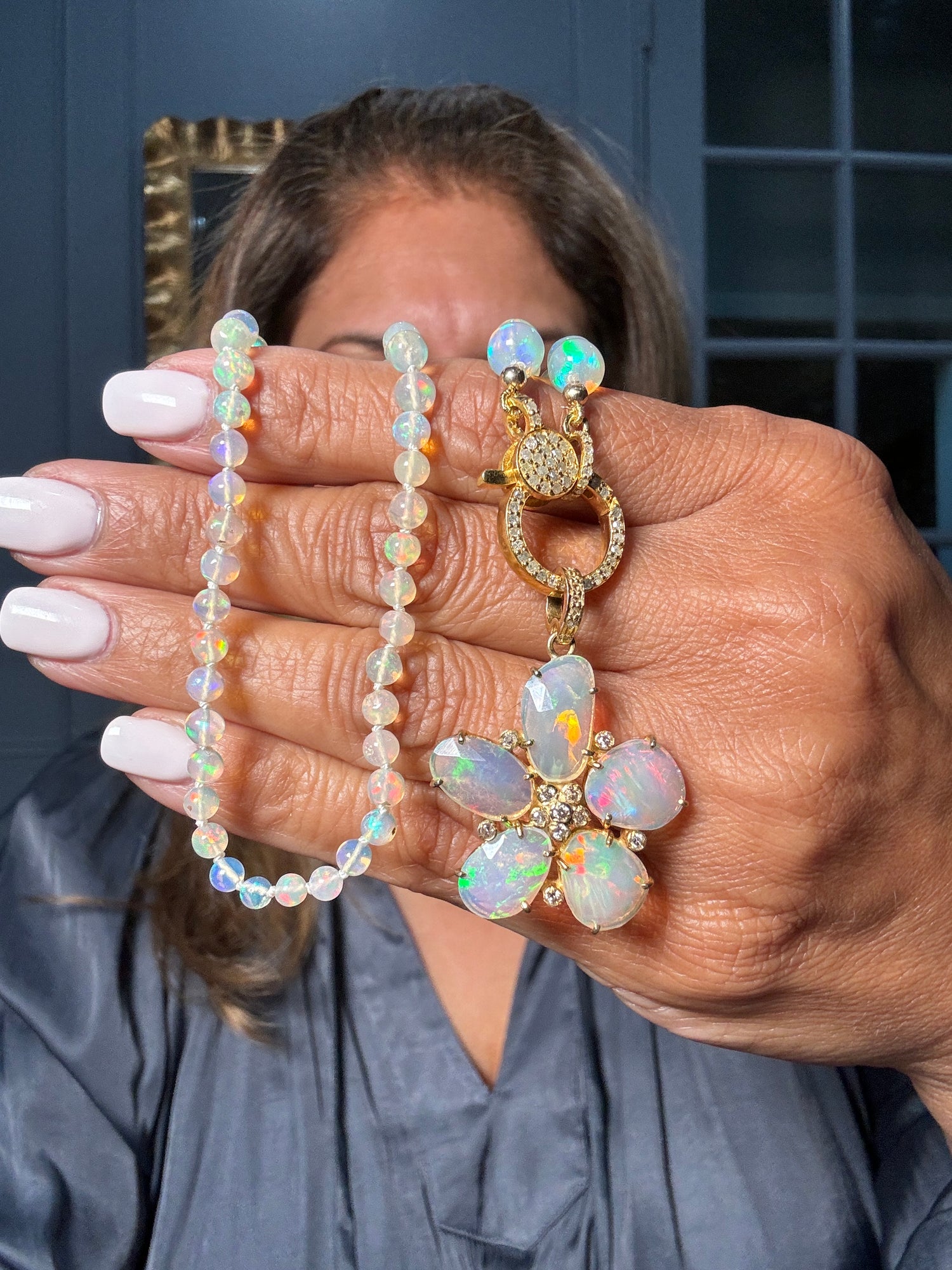 Ethiopian opal beads necklace with gold floral pendant featuring six oval opals and diamond accents, held in hand showing iridescent rainbow colors