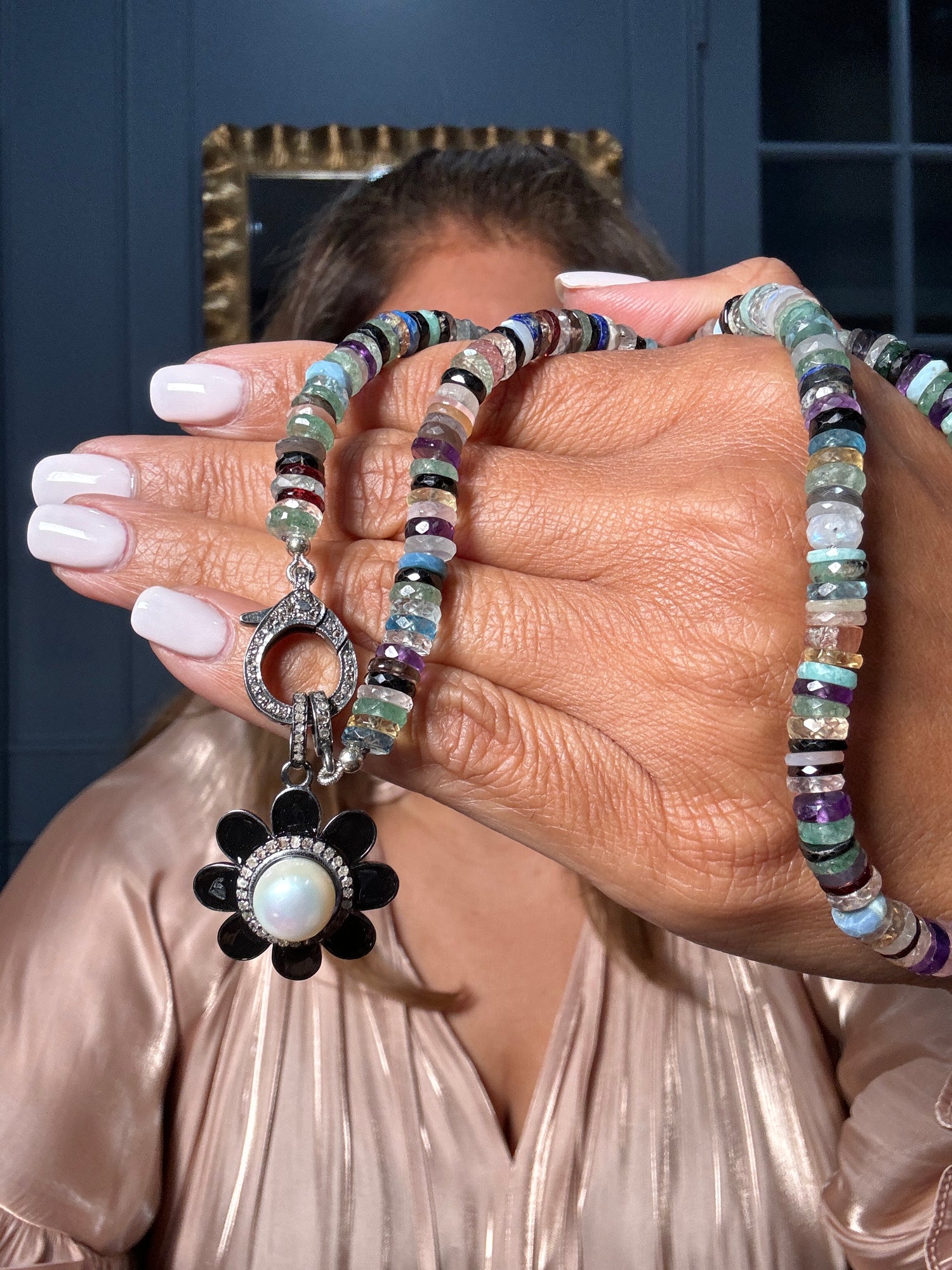 Woman's hands holding an 18-inch mixed gemstone necklace with multicolored tourmaline, amethyst, and fluorite beads featuring a black onyx flower pendant with pearl center and diamond clasp