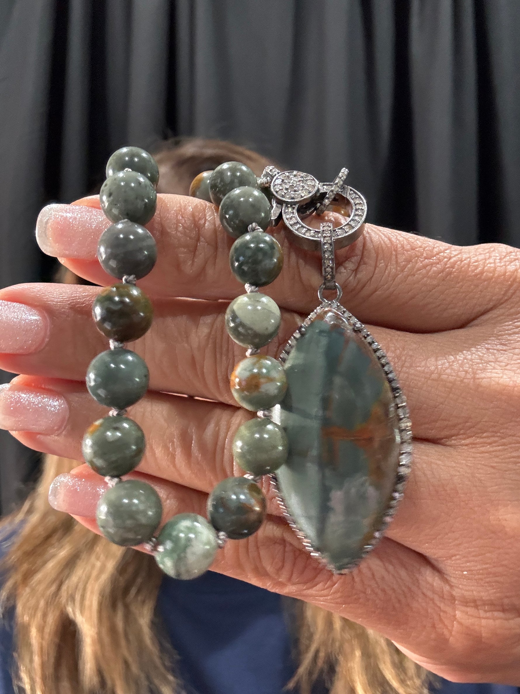 Hand displaying 18-inch Rocky Butte jasper bead necklace with green and brown tones, featuring diamond-accented sterling silver clasp and large marquise jasper pendant