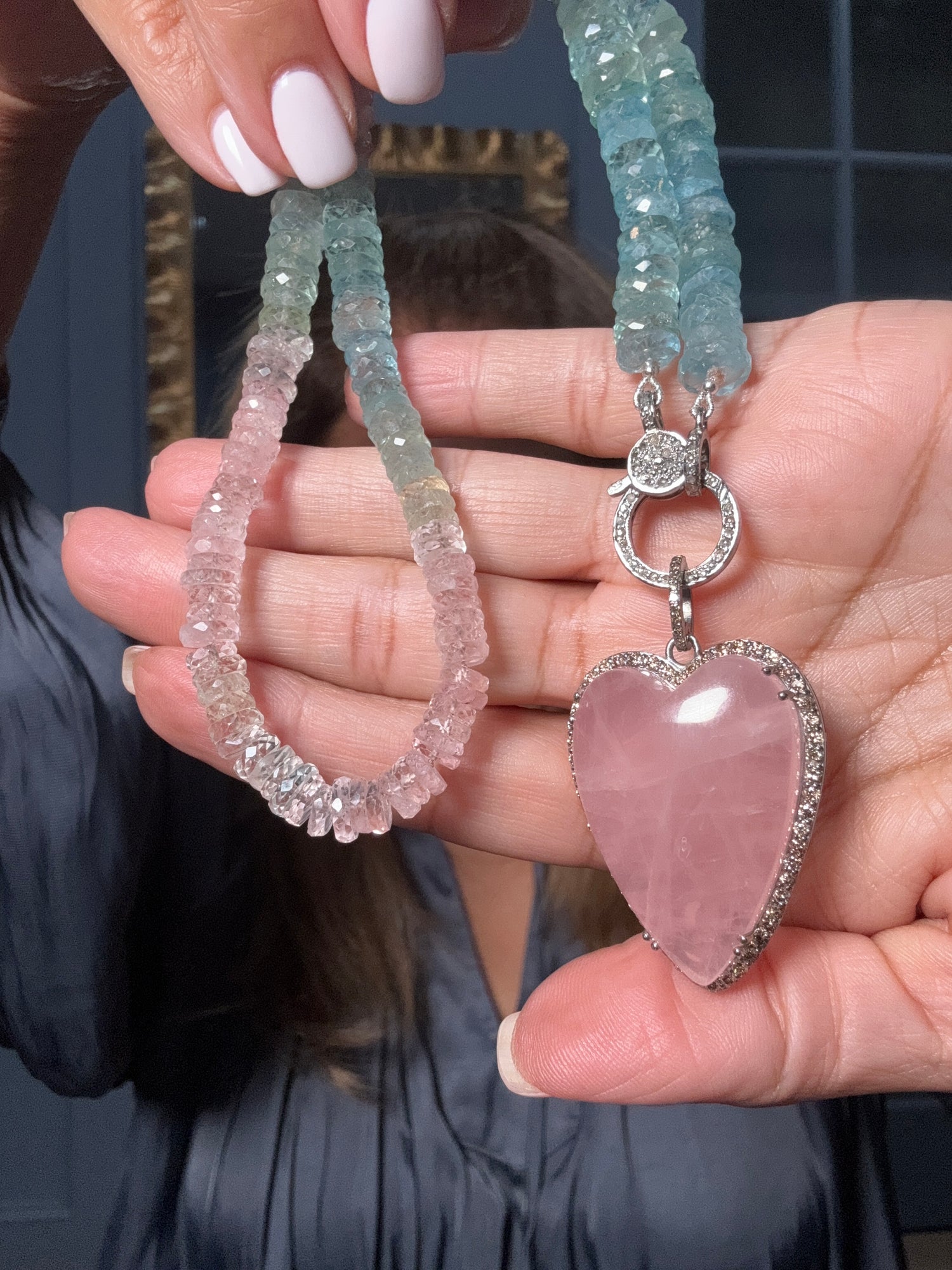 18-inch aquamarine and morganite beaded necklace held in hands, featuring blue-green and pink faceted gemstones with sterling silver diamond clasp and rose quartz heart pendant.