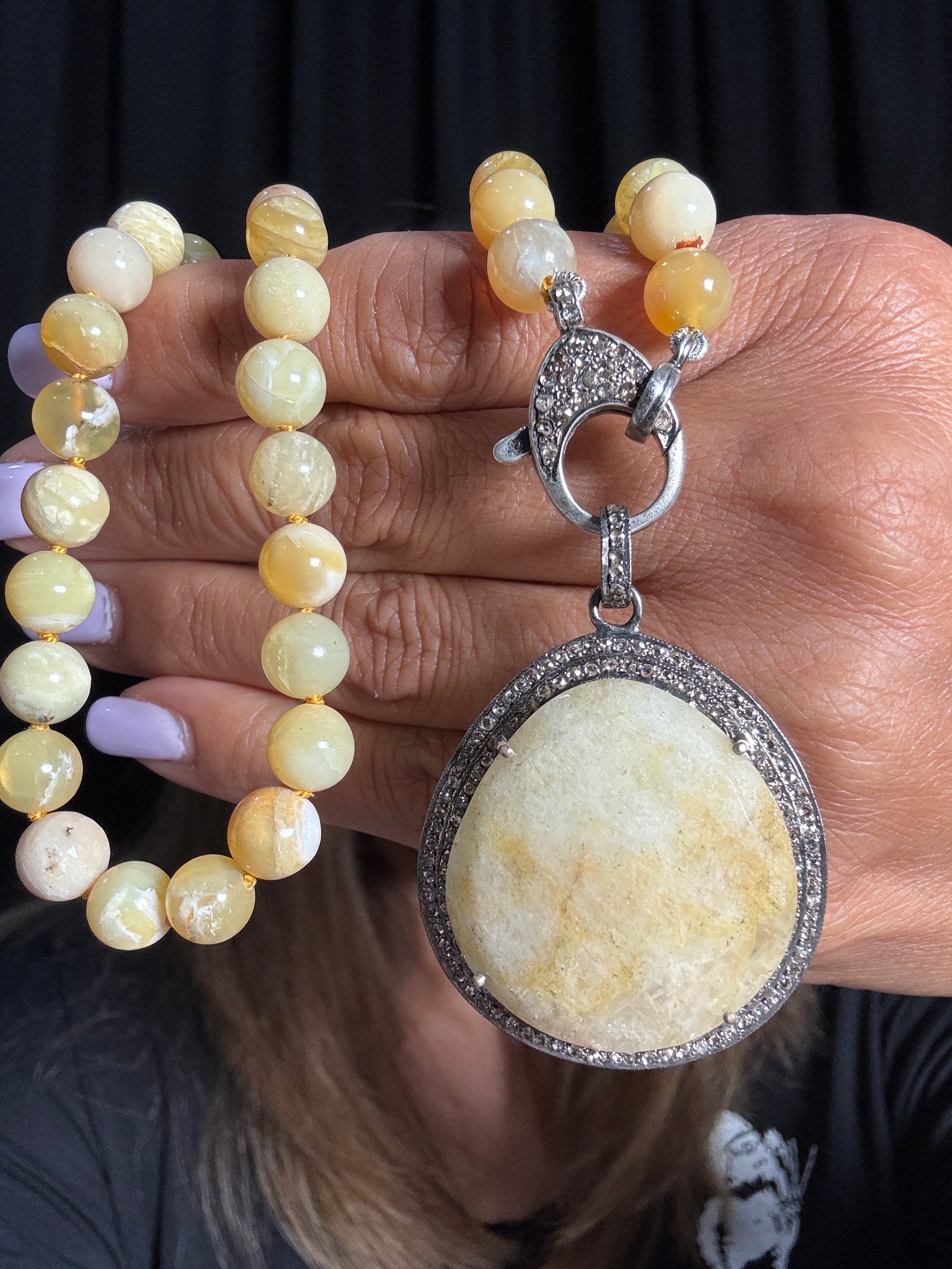 Hand holding an 18-inch yellow opal beaded necklace with large circular yellow aquamarine pendant surrounded by diamonds in sterling silver setting