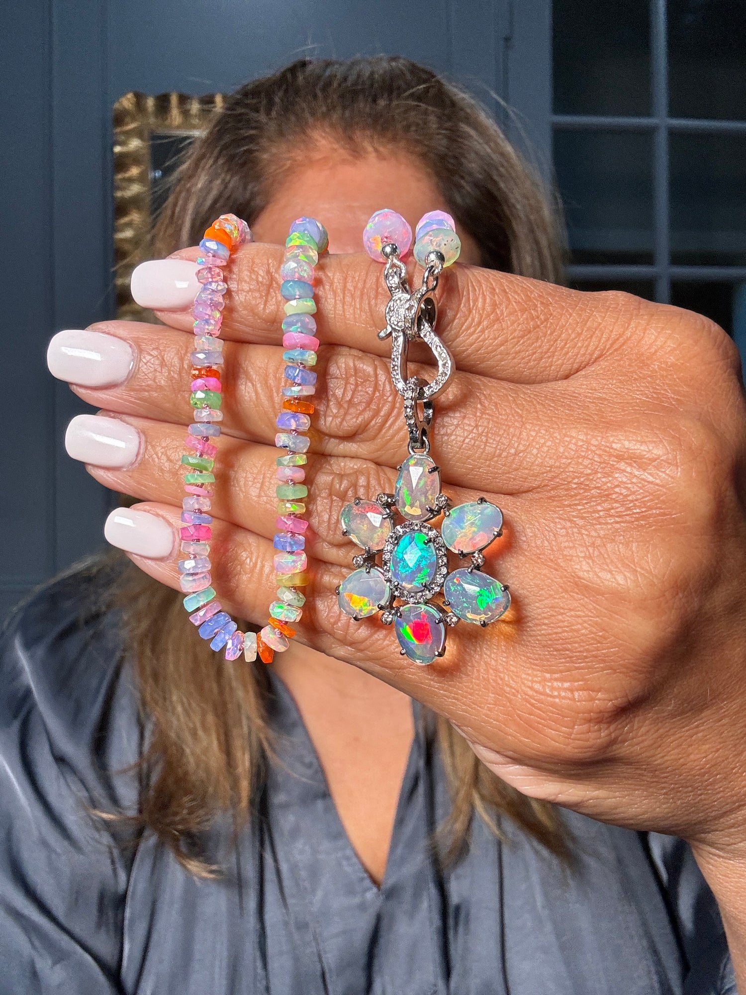 Hand displaying vibrant Ethiopian opal beads with iridescent rainbow flashes alongside sterling silver flower pendant featuring multiple opals and diamonds in center
