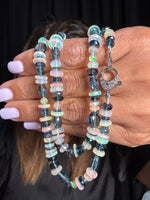 Hands holding a 21-inch Ethiopian opal and London blue topaz necklace with iridescent white opal discs and deep blue faceted gemstones, featuring an ornate sterling silver toggle clasp