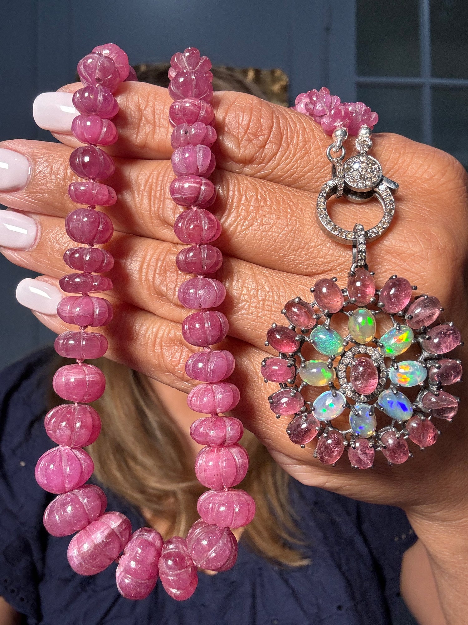 Hand holding 22-inch carved pink tourmaline bead necklace with sterling silver diamond clasp and large flower-shaped pendant featuring pink tourmalines and opals