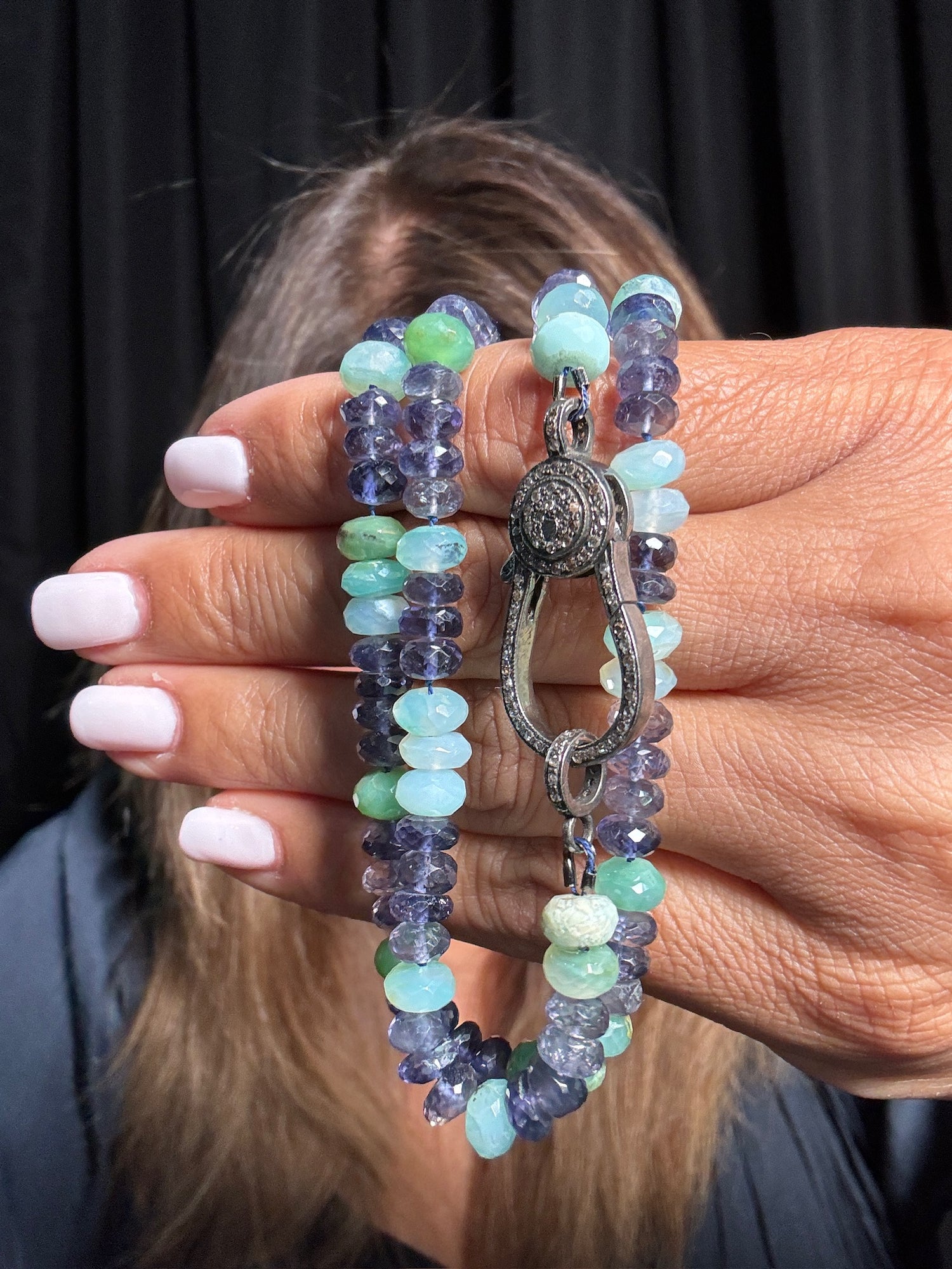 Hand holding 24-inch iolite and Peruvian opal necklace with purple and mint green faceted gemstone beads, featuring ornate silver clasp with diamond accents