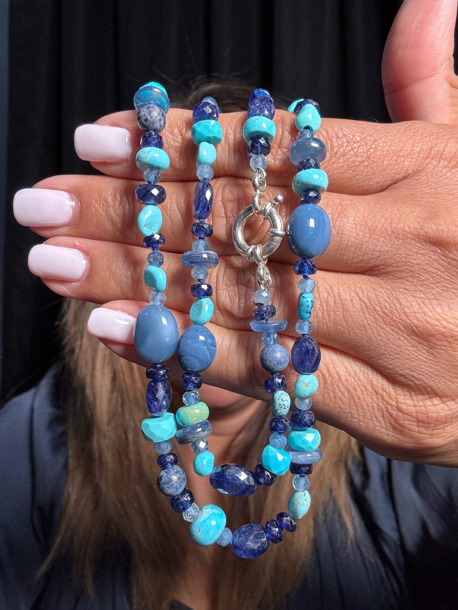Hand holding 26-inch beaded necklace with turquoise, blue kyanite, and sapphire gemstones in various shapes with sterling silver toggle clasp