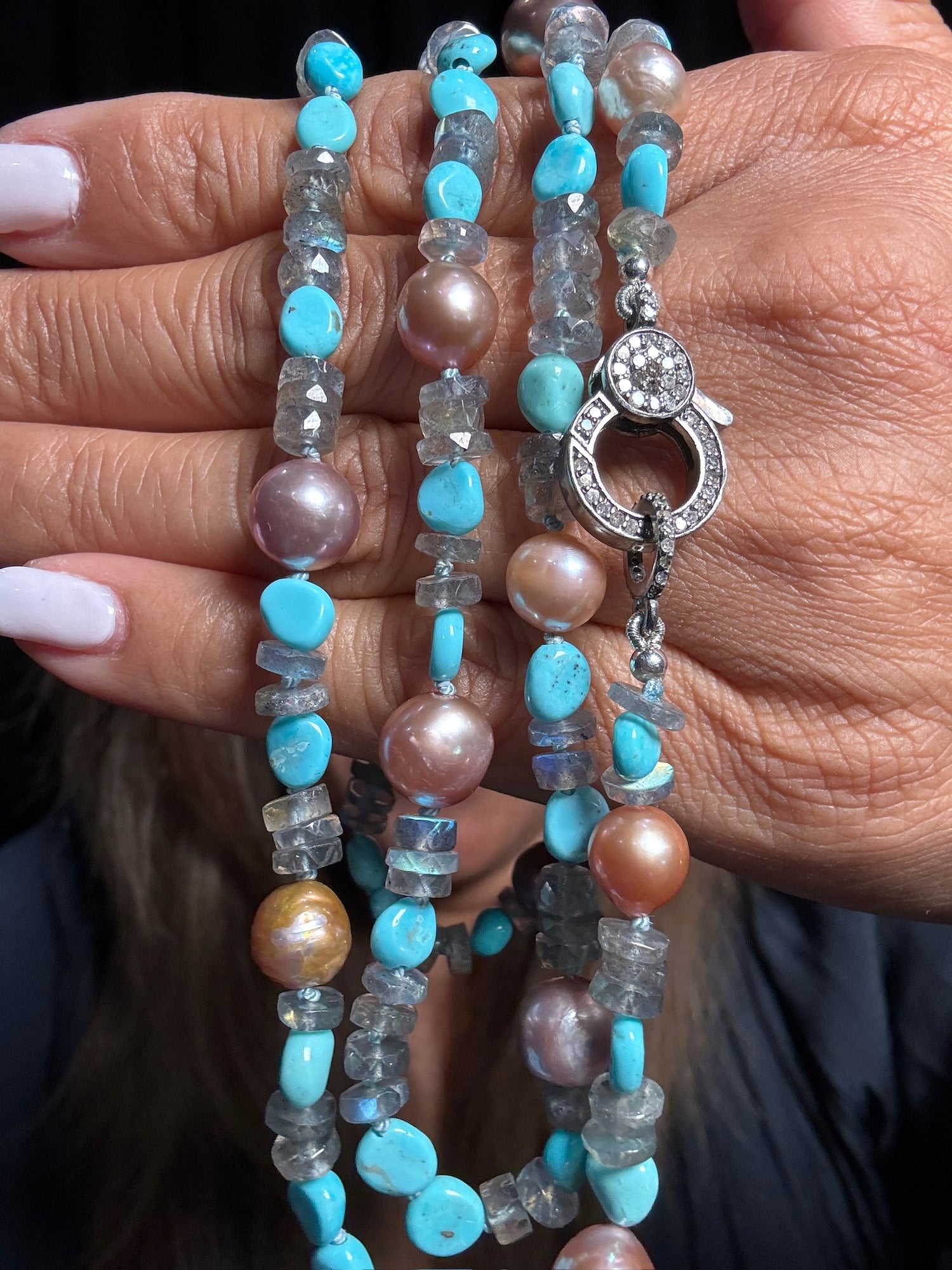 Close-up of 34-inch beaded necklace held in hands, featuring turquoise stones, labradorite chips, pink-brown pearls, and sterling silver diamond clasp