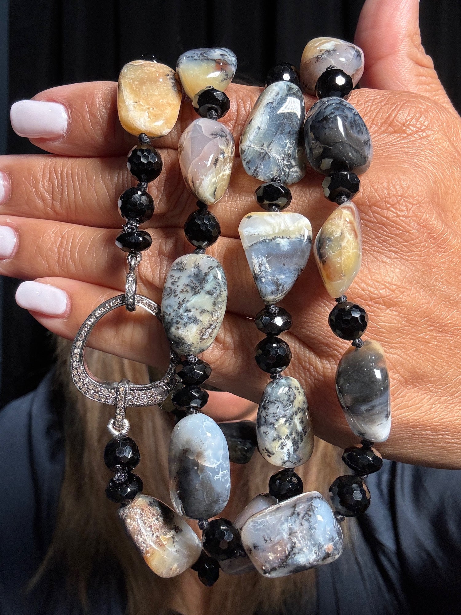 Person holding 36-inch dendrite opal and black spinel necklace featuring marbled gray cream stones with diamond-encrusted sterling silver circle clasp