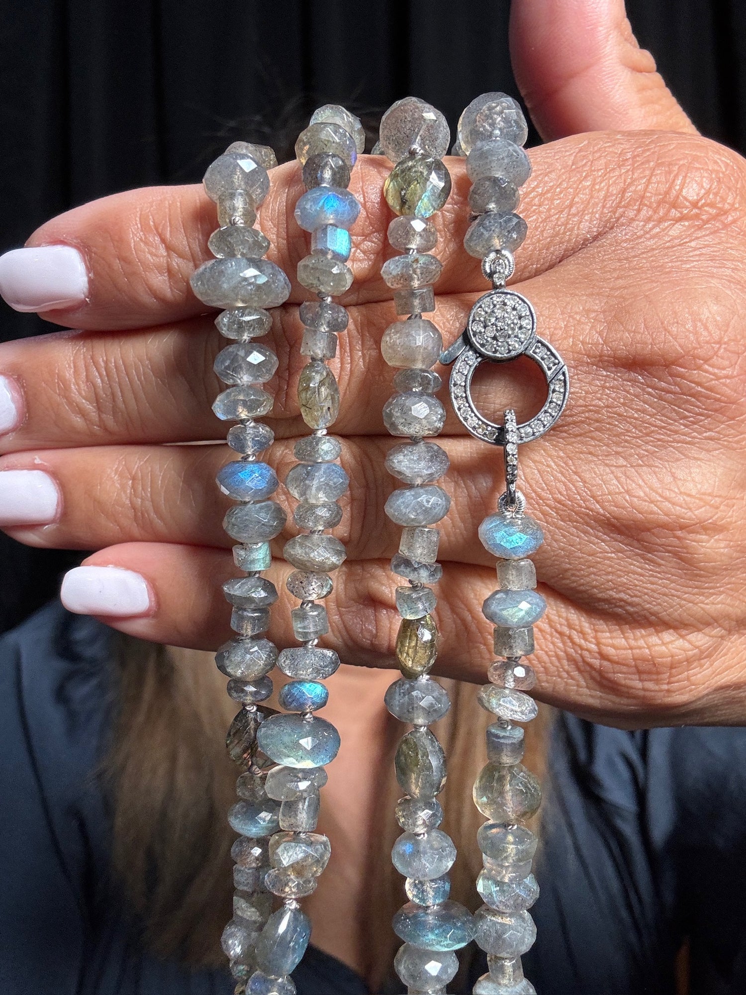 Hand holding a 36-inch labradorite necklace with faceted gray stones showing blue flash and diamond-accented sterling silver clasp