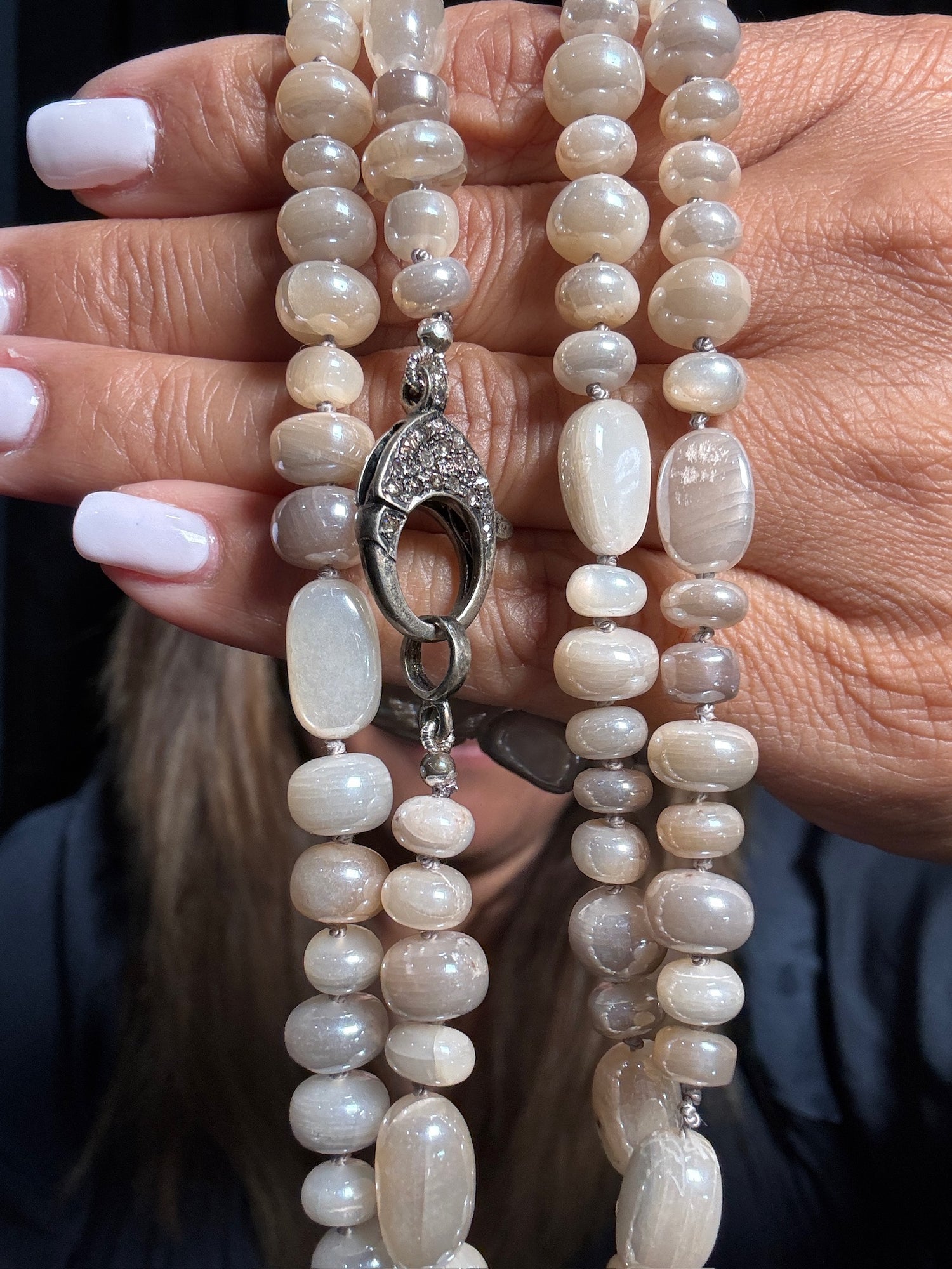 Hands holding 36-inch polished moonstone necklace with cream and gray oval beads, featuring ornate silver clasp with crystal details