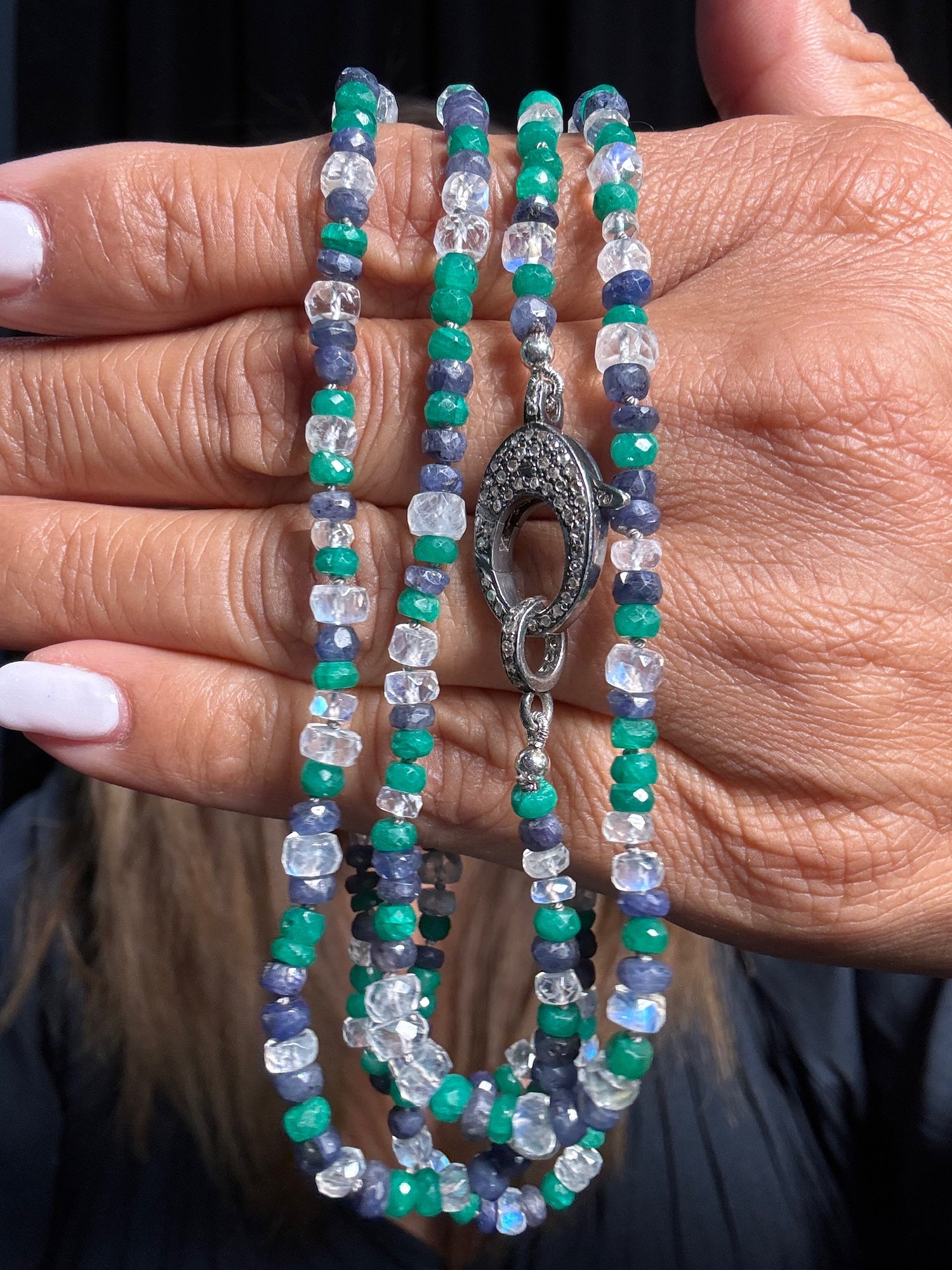 Hand holding 37-inch necklace with faceted moonstone, green onyx, and blue sapphire beads featuring ornate silver clasp with dark center stone