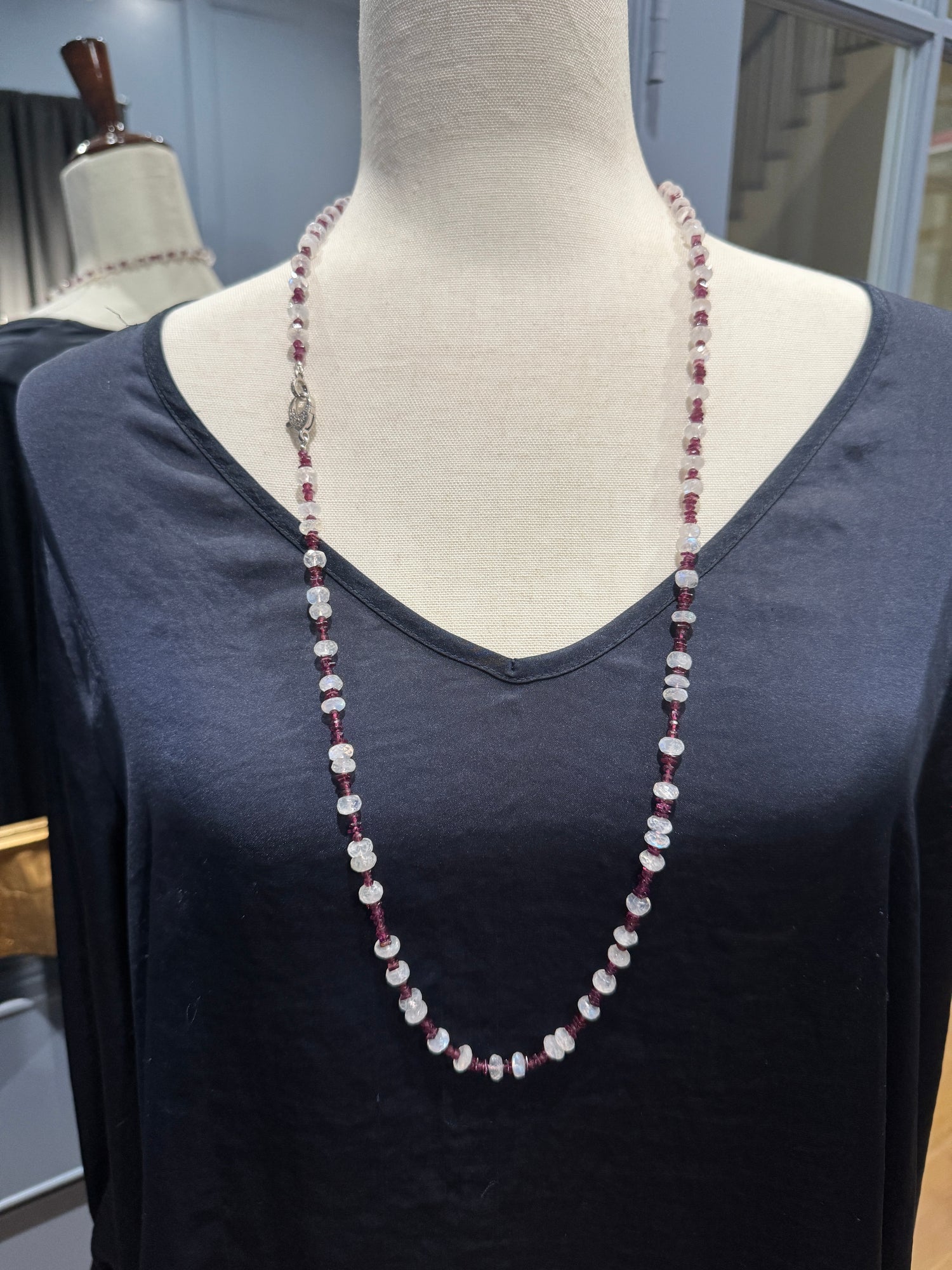Long 34-inch rhodolite garnet and moonstone necklace displayed on black v-neck mannequin, showing alternating purple-red garnet chips and translucent white moonstone coins
