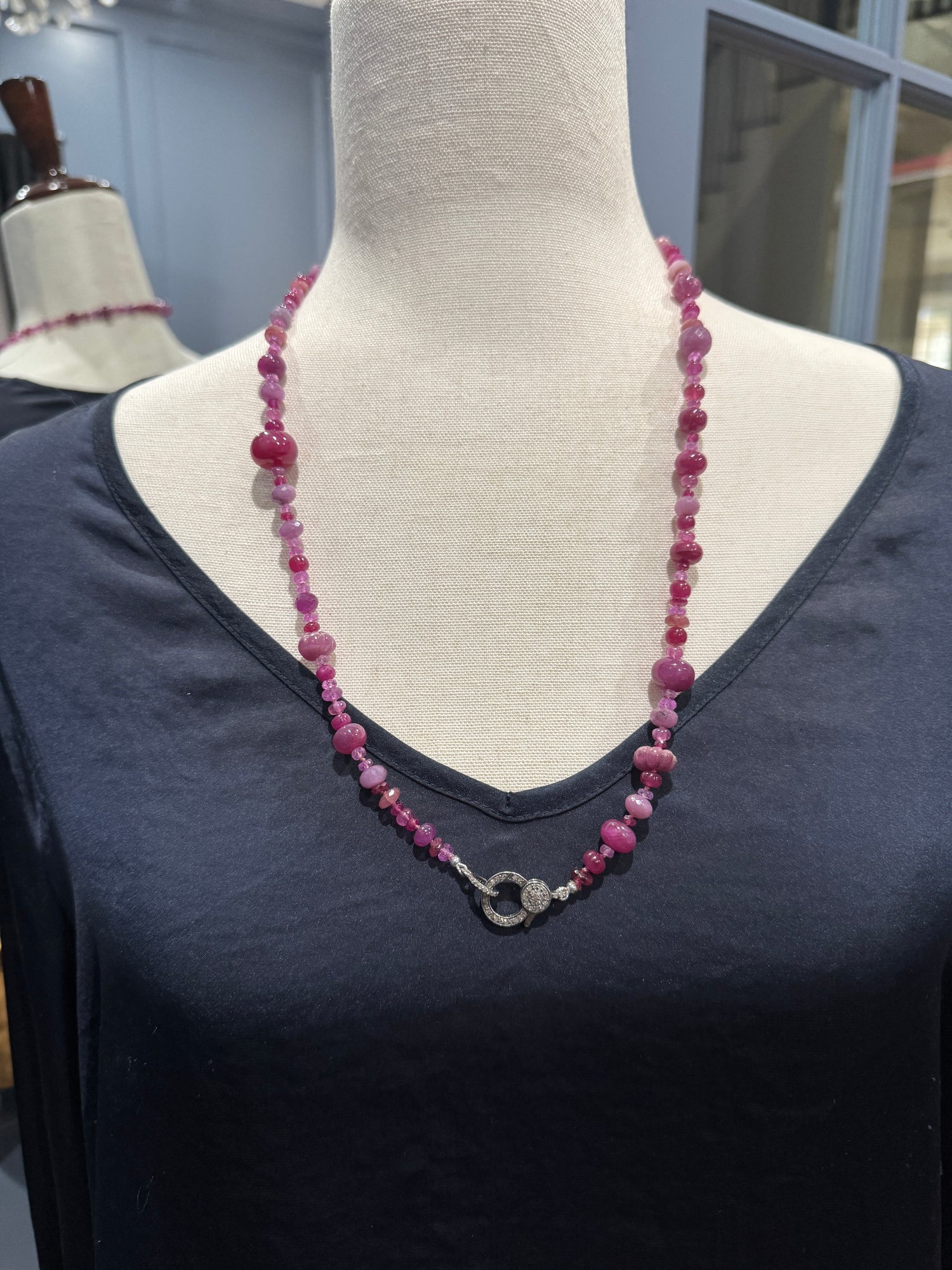 26-inch ruby sapphire necklace displayed on cream fabric mannequin showing graduated pink and red gemstones with sparkly diamond clasp