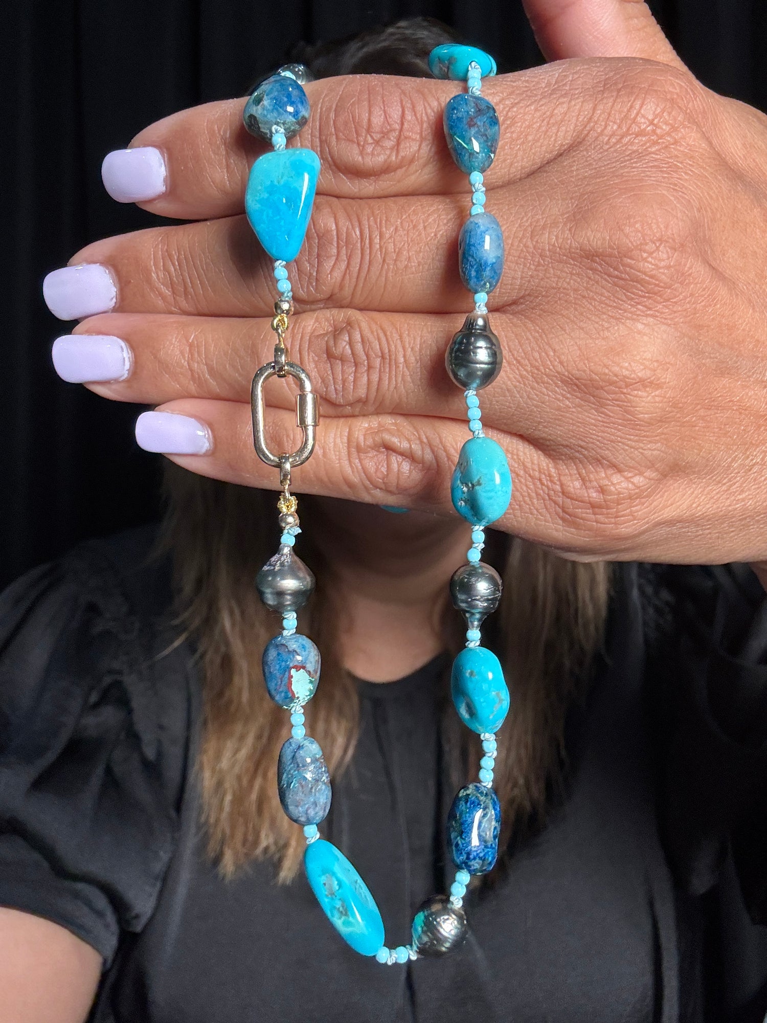 18-inch Tahitian pearl and turquoise necklace held in hand showing bright blue Sleeping Beauty turquoise nuggets, deep blue chrysocolla beads, dark Tahitian pearls, and 14k gold carabiner clasp