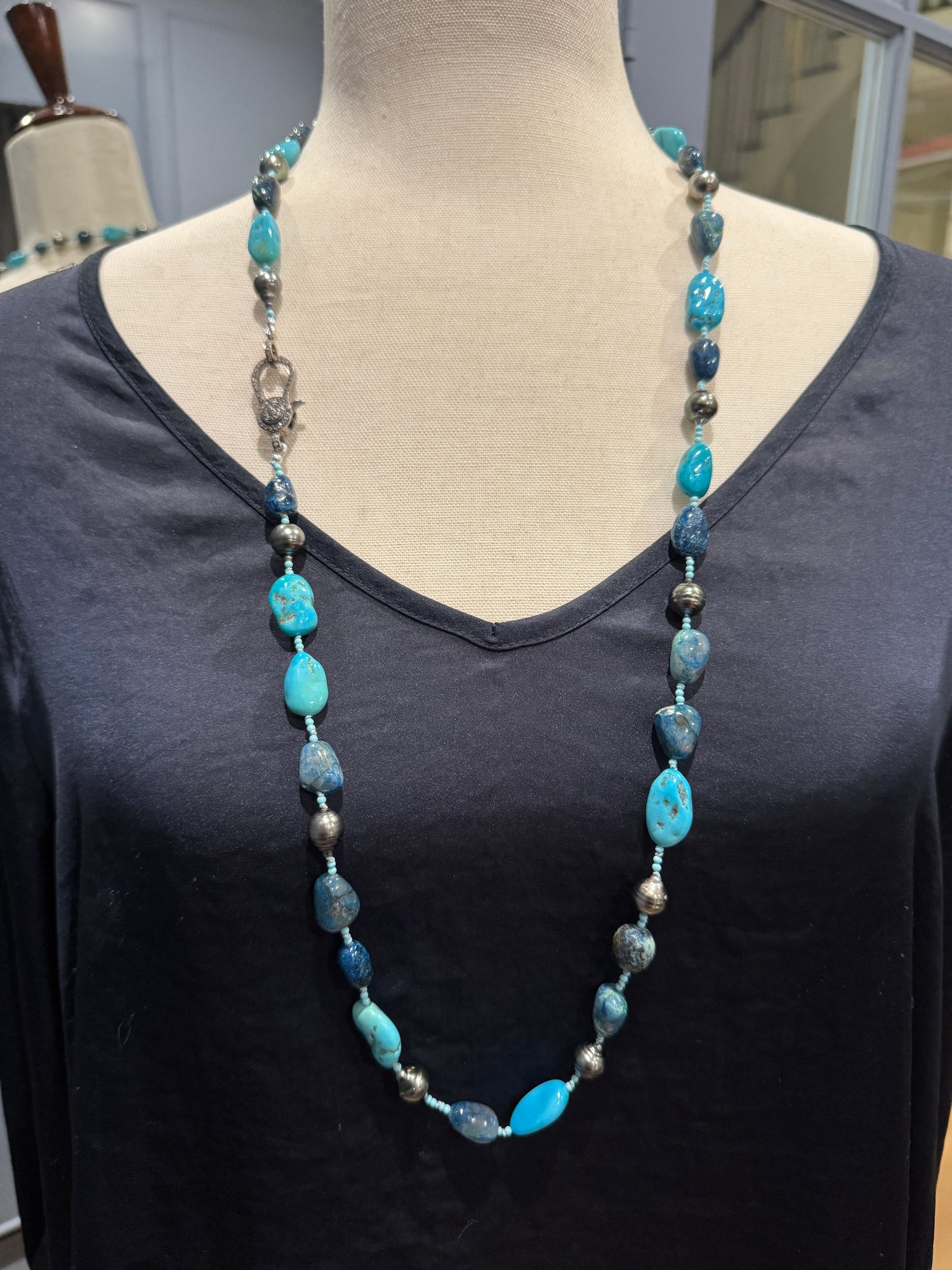 Long turquoise and Tahitian pearl necklace displayed on neutral mannequin, showing mixed blue gemstones and gray pearls