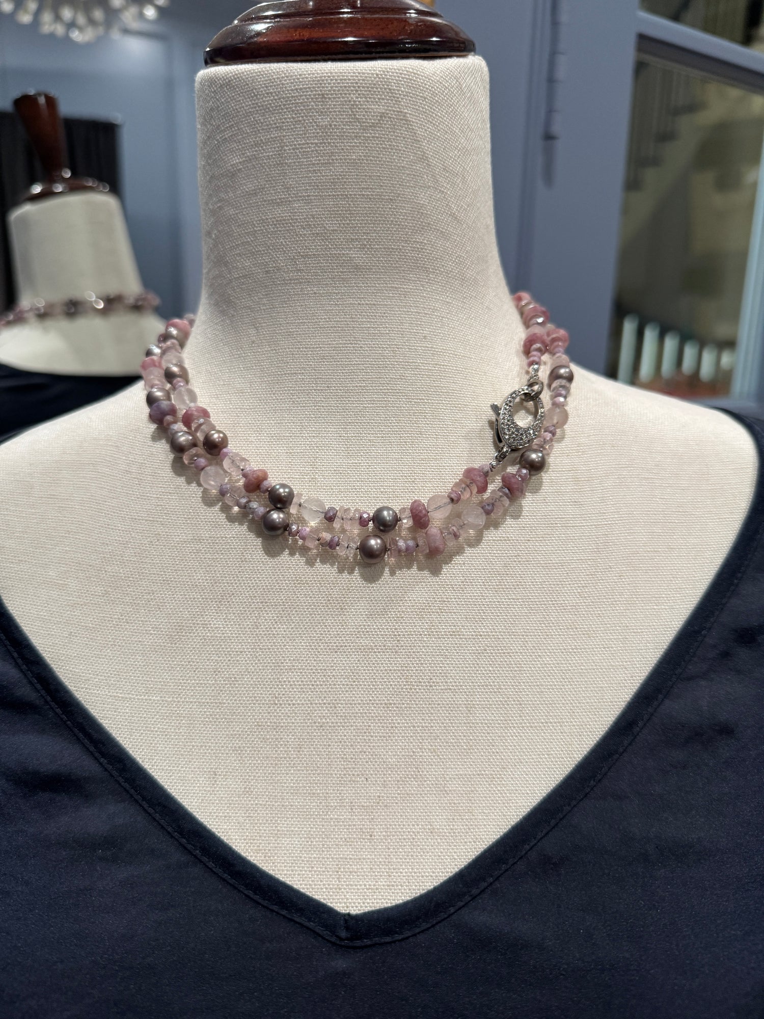 Long pink gemstone and gray Tahitian pearl necklace displayed on cream fabric mannequin, showing elegant drape and mixed stone textures