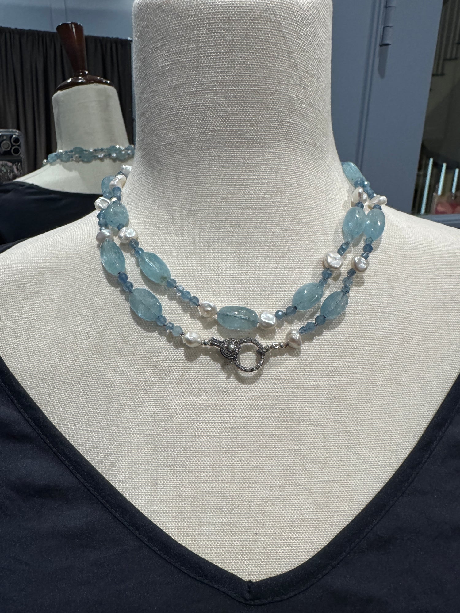 Double-strand aquamarine and pearl necklace displayed on beige mannequin showing oval blue gemstones alternating with white baroque pearls