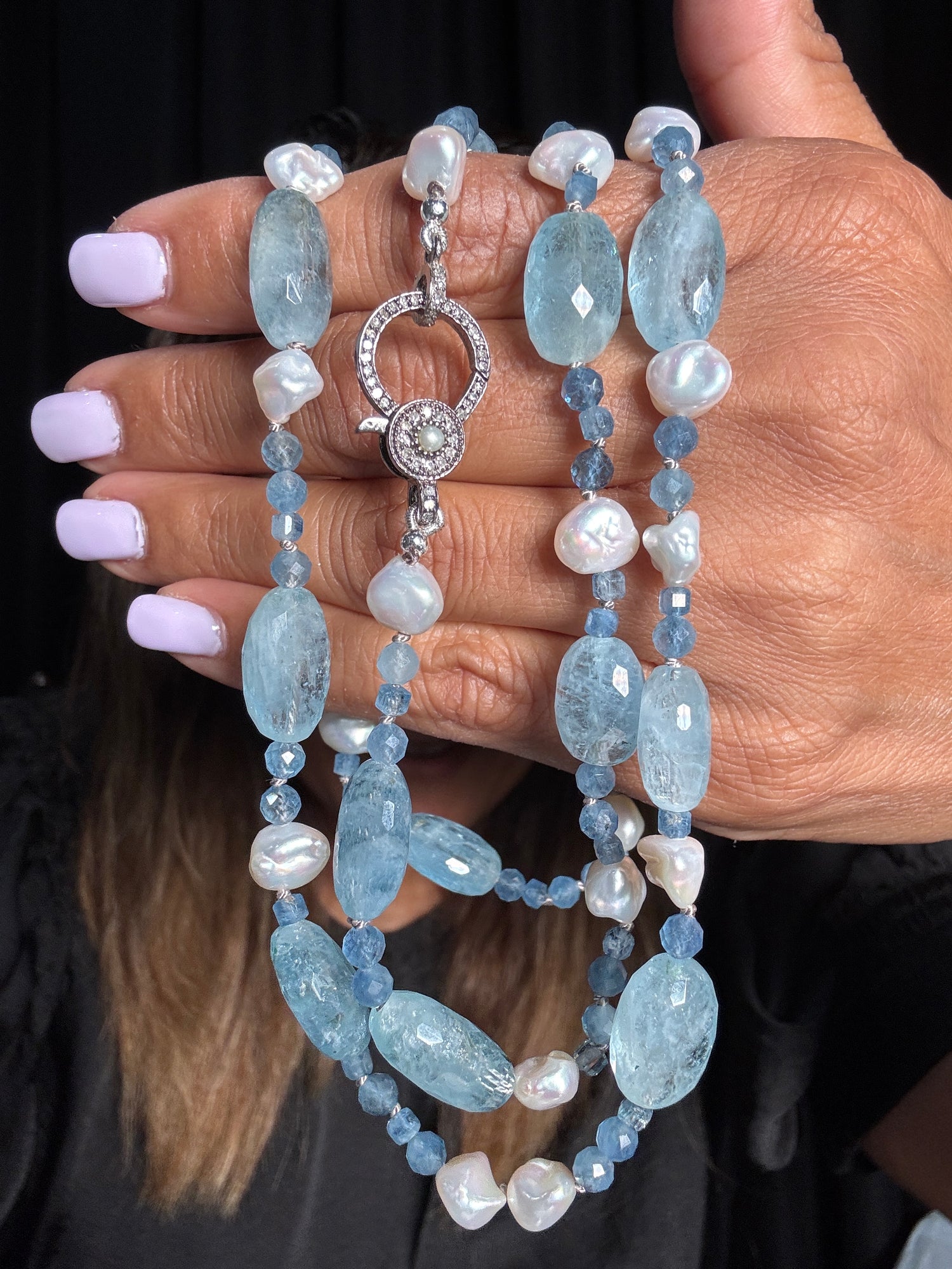 Hand holding 36-inch necklace with pale blue oval Santa Maria aquamarine stones and white baroque keshi pearls with sterling silver diamond clasp