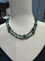 Close-up view of grandidierite and Tahitian pearl necklace on mannequin displaying teal gemstone beads and dark gray baroque pearls in choker-style wrap