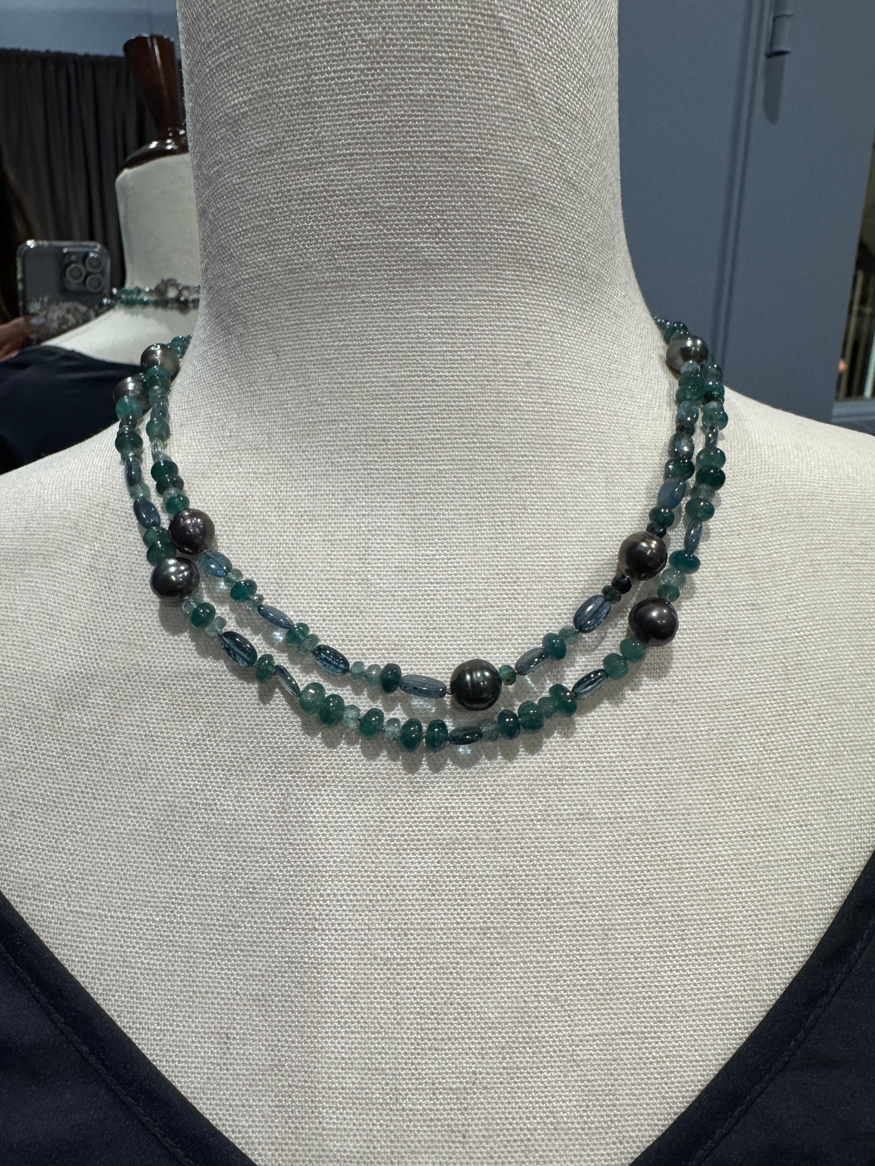 Close-up view of grandidierite and Tahitian pearl necklace on mannequin displaying teal gemstone beads and dark gray baroque pearls in choker-style wrap