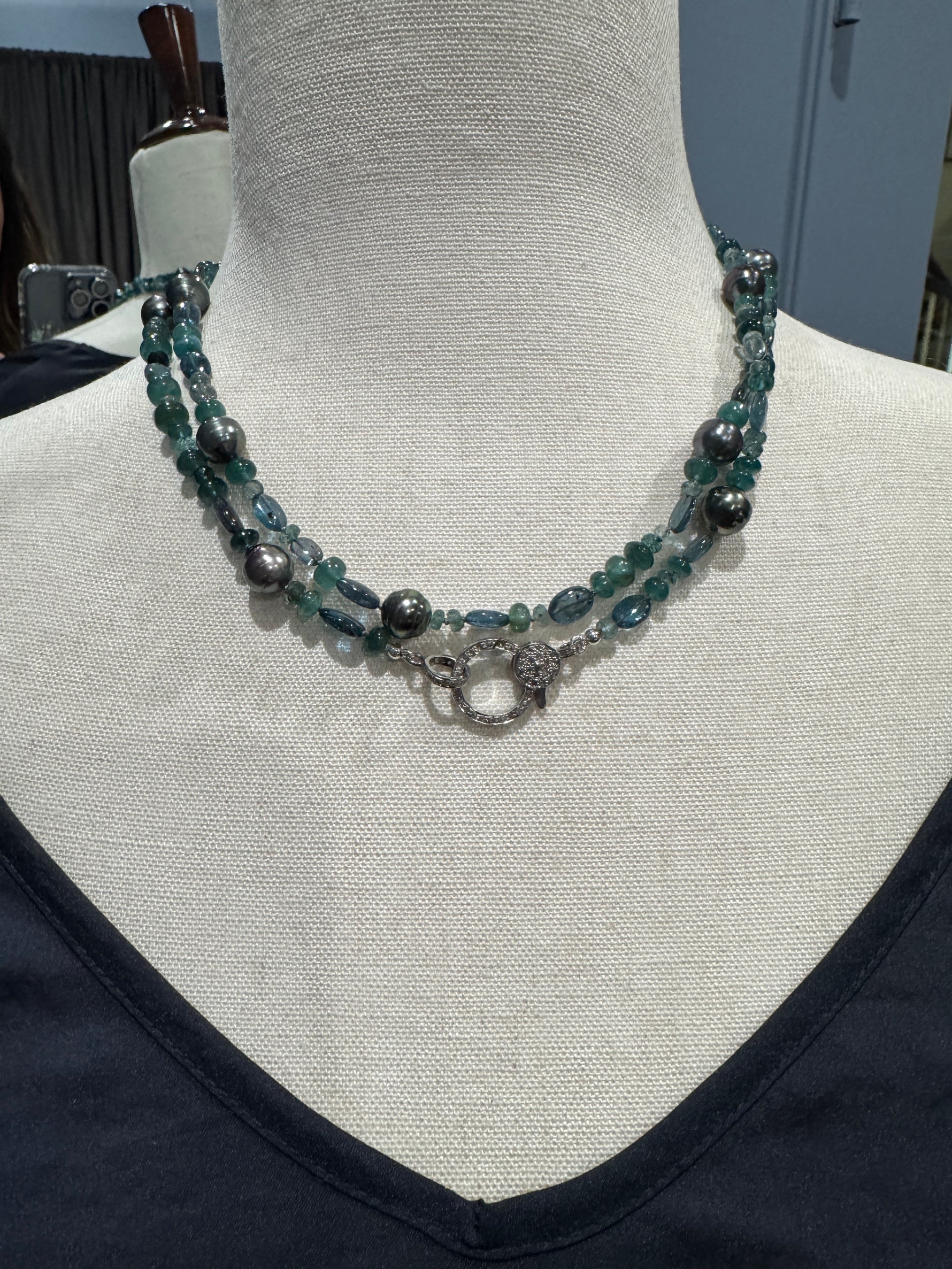 36-inch grandidierite and Tahitian pearl necklace displayed on beige fabric mannequin showing double-wrap styling with teal gemstones and dark Tahitian pearls