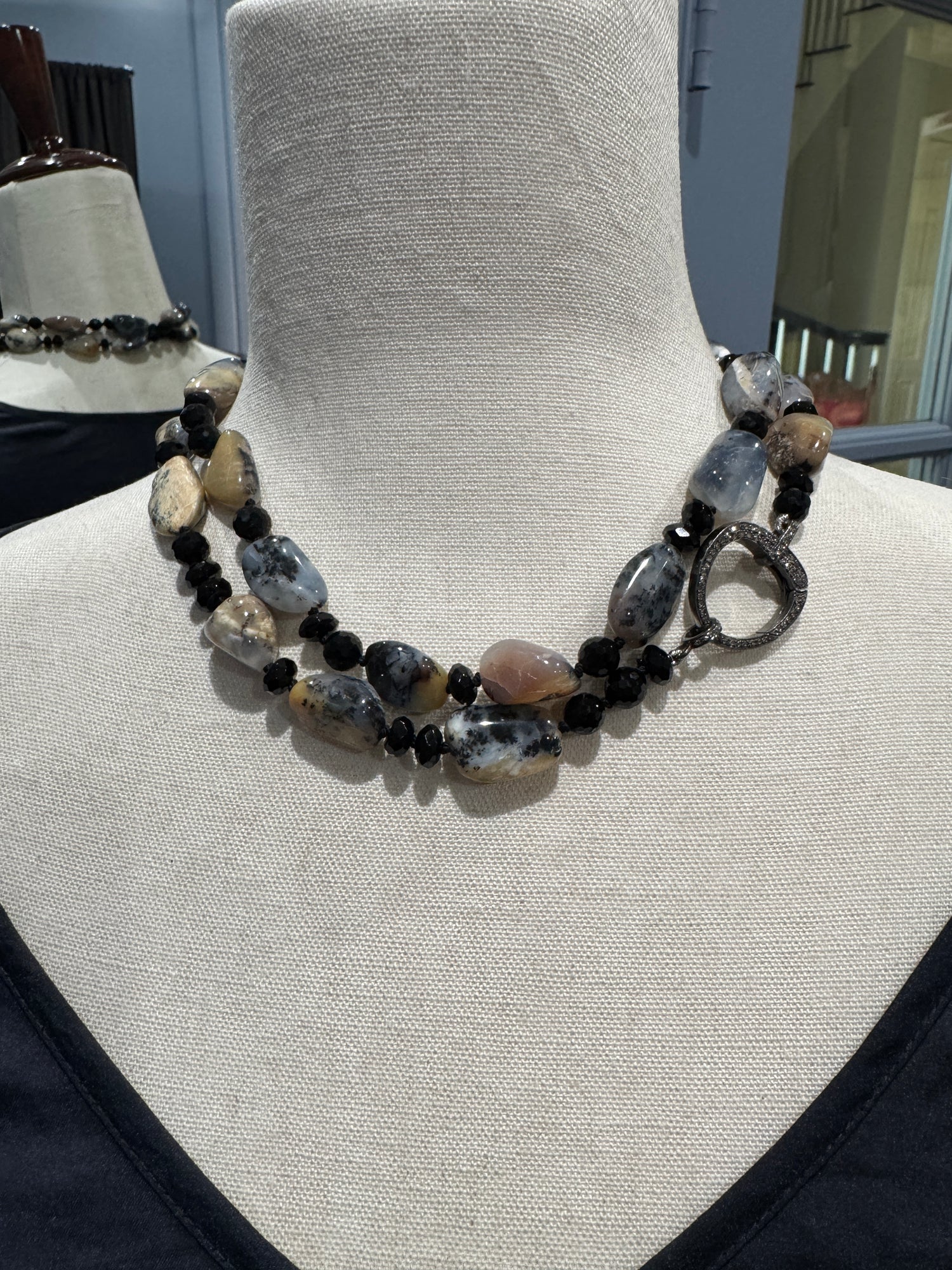 Dendrite opal and black spinel necklace displayed on beige mannequin showing natural stone variations and sparkling circular clasp detail