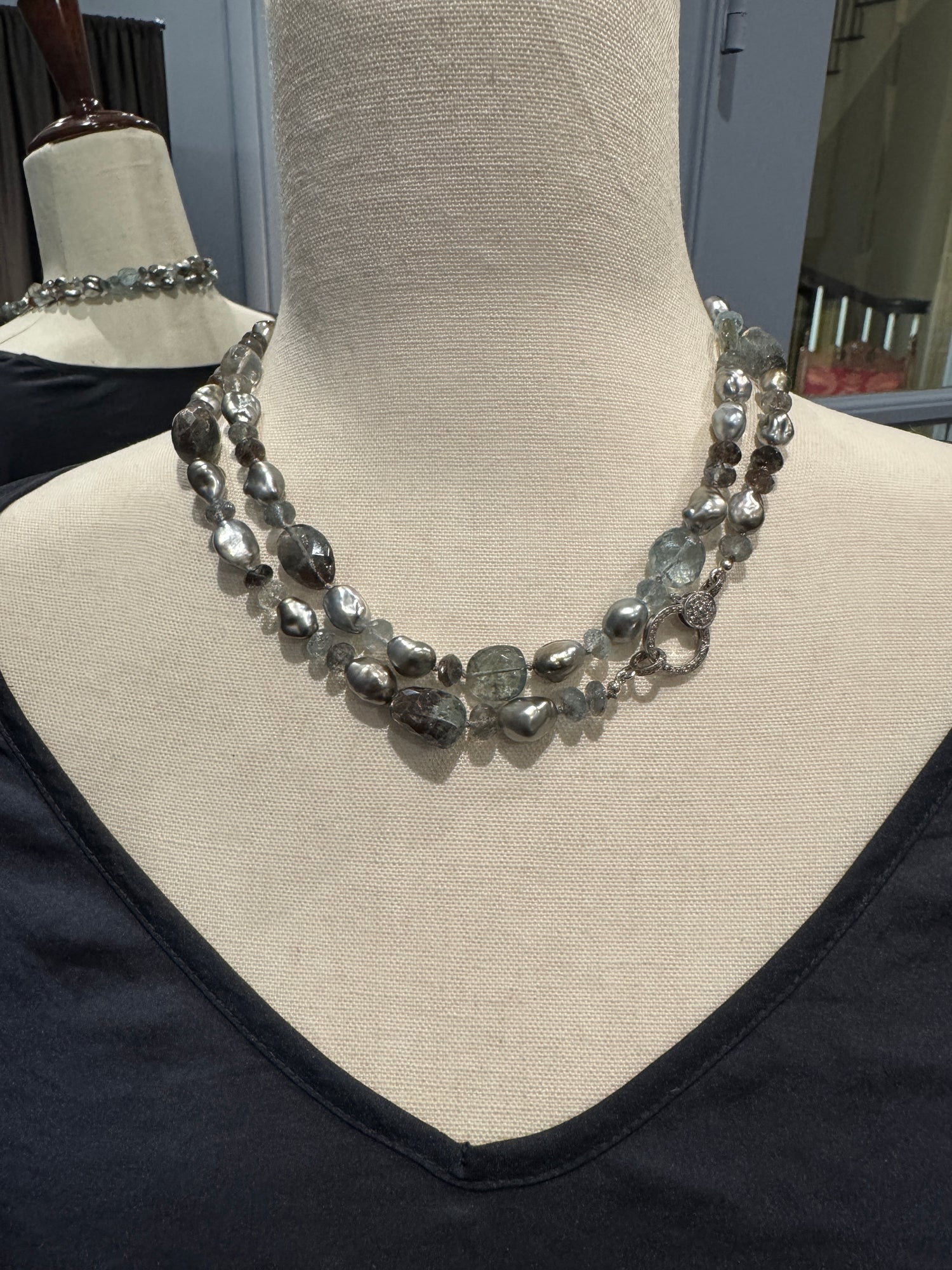 Luxurious double-strand necklace displaying copper aquamarine stones and gray Tahitian keshi pearls with silver diamond clasp, styled on fabric mannequin bust