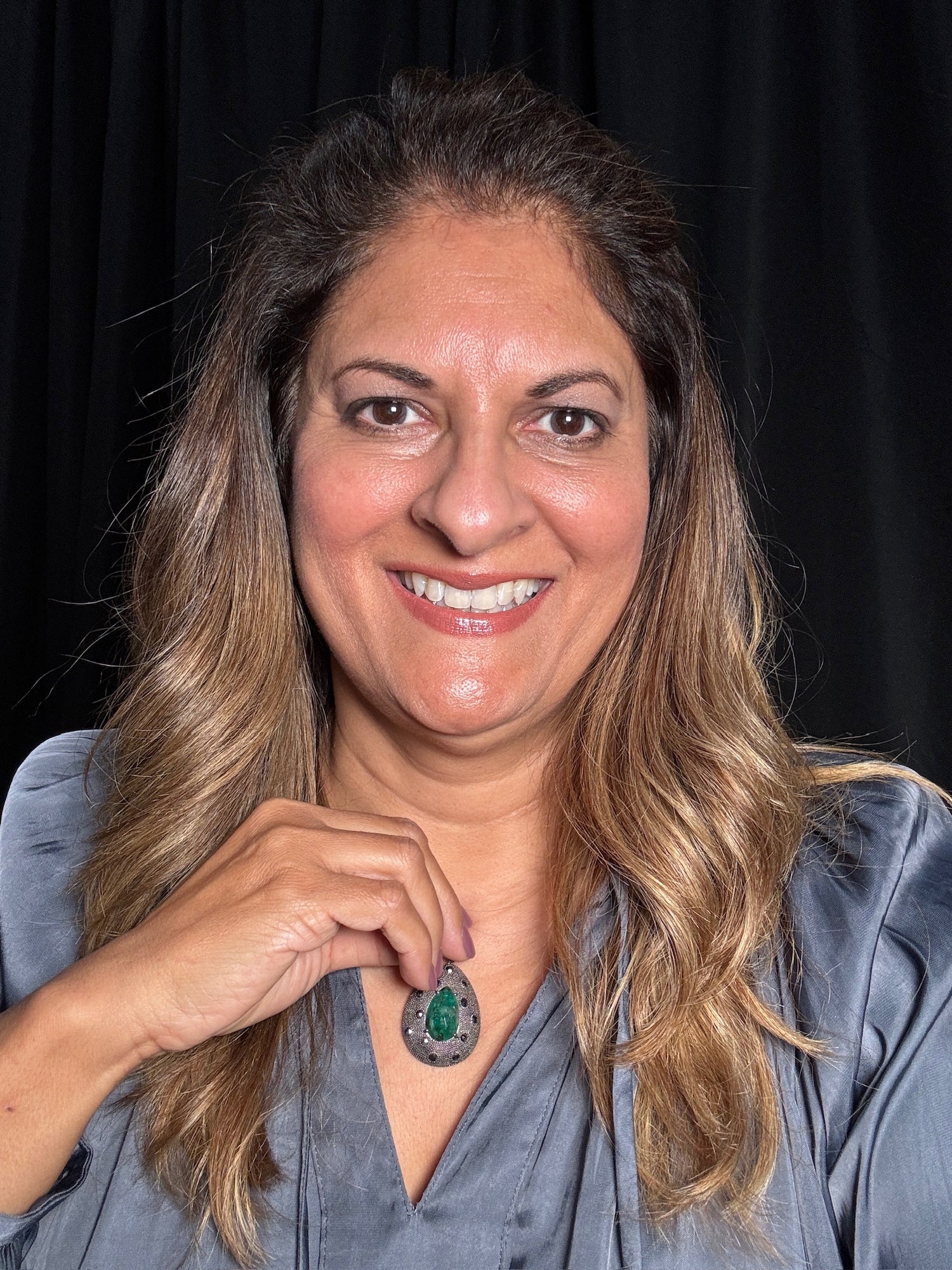 Smiling woman wearing teardrop emerald and diamond pendant in sterling silver, displaying the luxurious gemstone jewelry piece