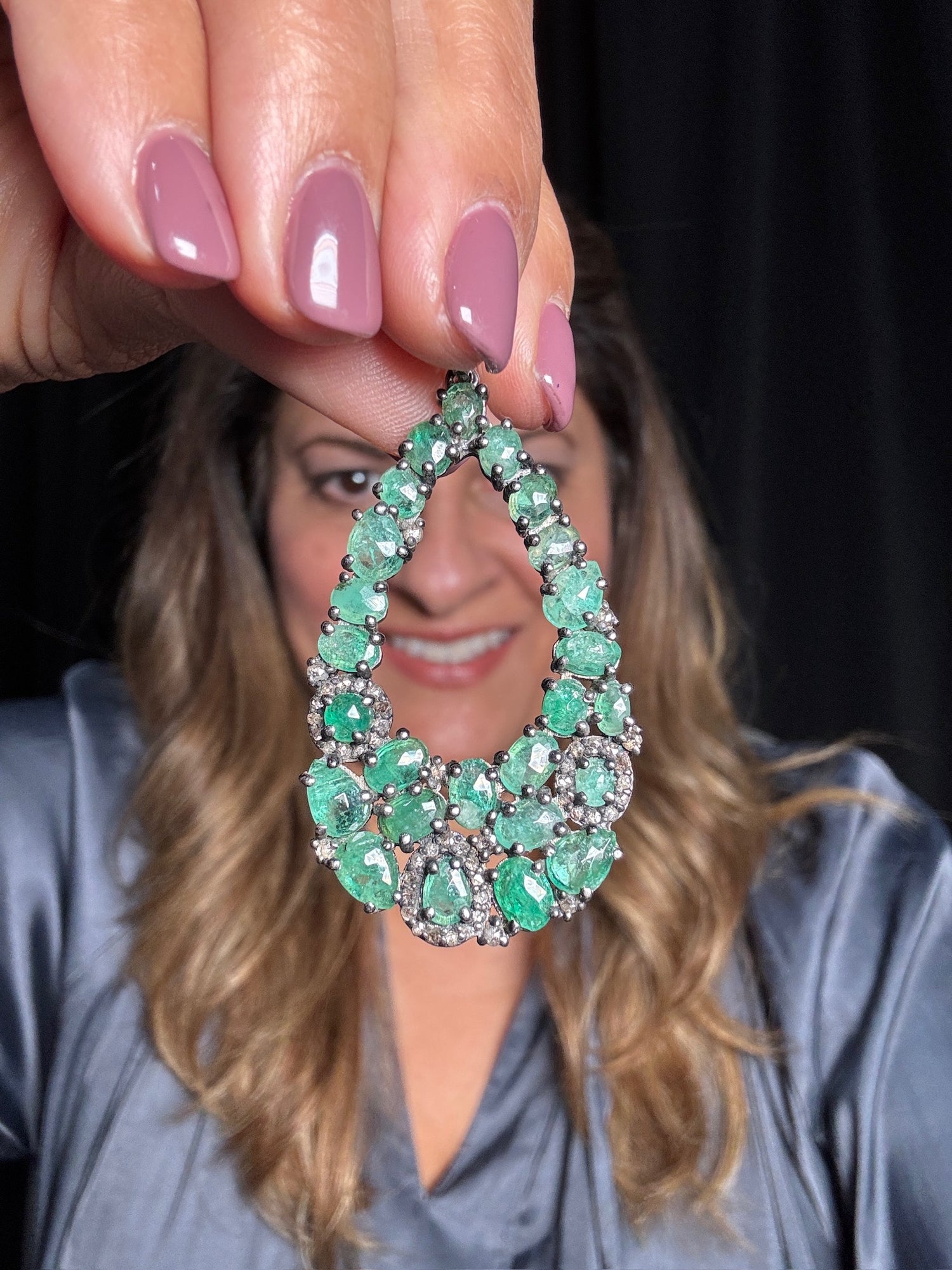 Hand holding ornate emerald and diamond teardrop pendant featuring multiple oval emeralds with diamond accents in sterling silver setting