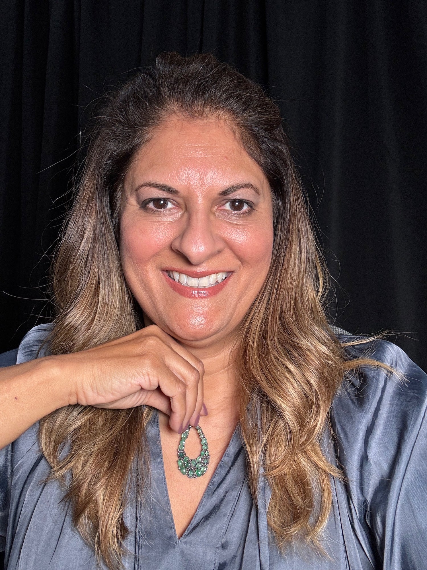 Woman wearing emerald and diamond teardrop pendant necklace in sterling silver, showcasing the intricate gemstone arrangement against gray blouse