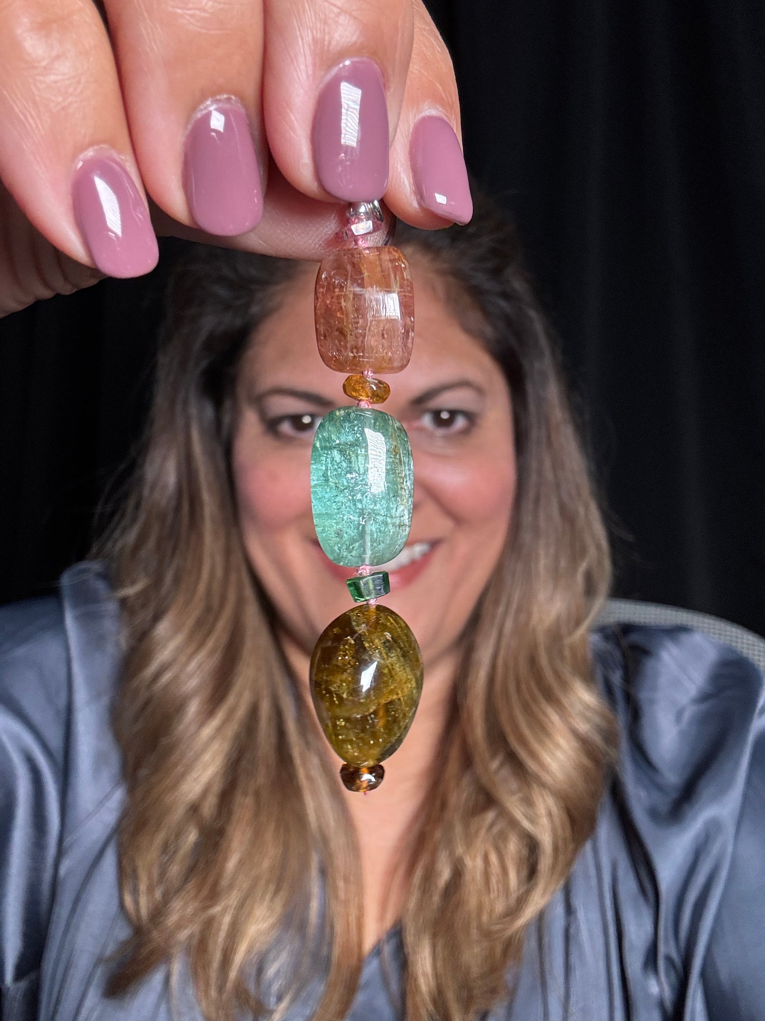 Hand holding multi-colored tourmaline drop pendant featuring stacked oval stones in peach, green and amber with silver spacers