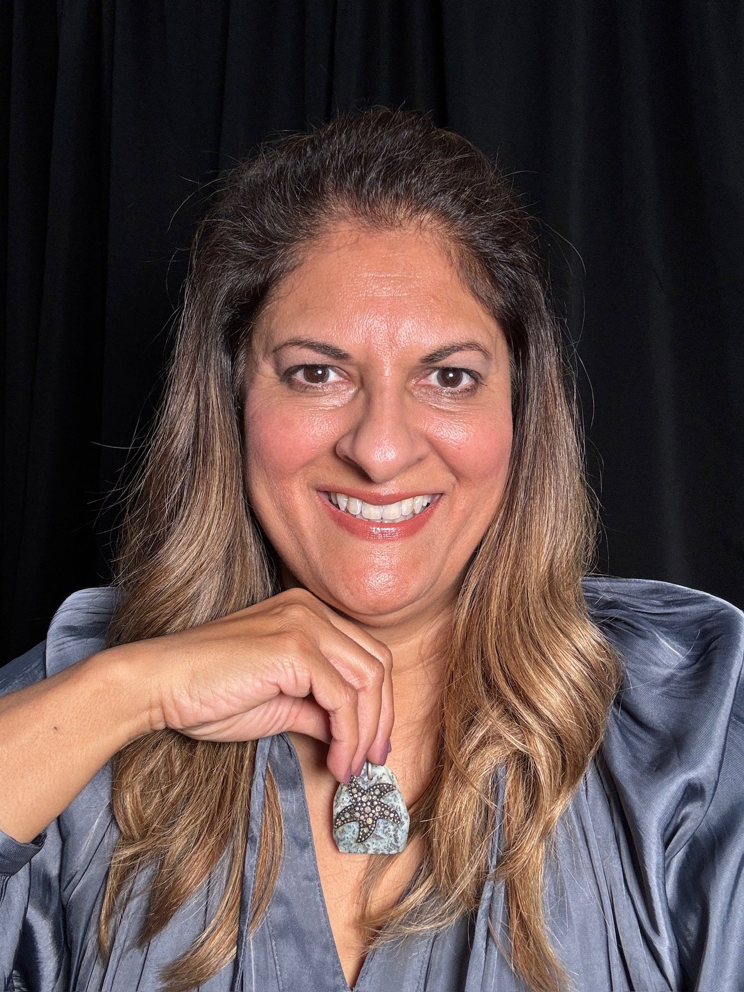 Smiling woman wearing gray shirt displays white African opal starfish pendant with sparkling diamonds on sterling silver chain