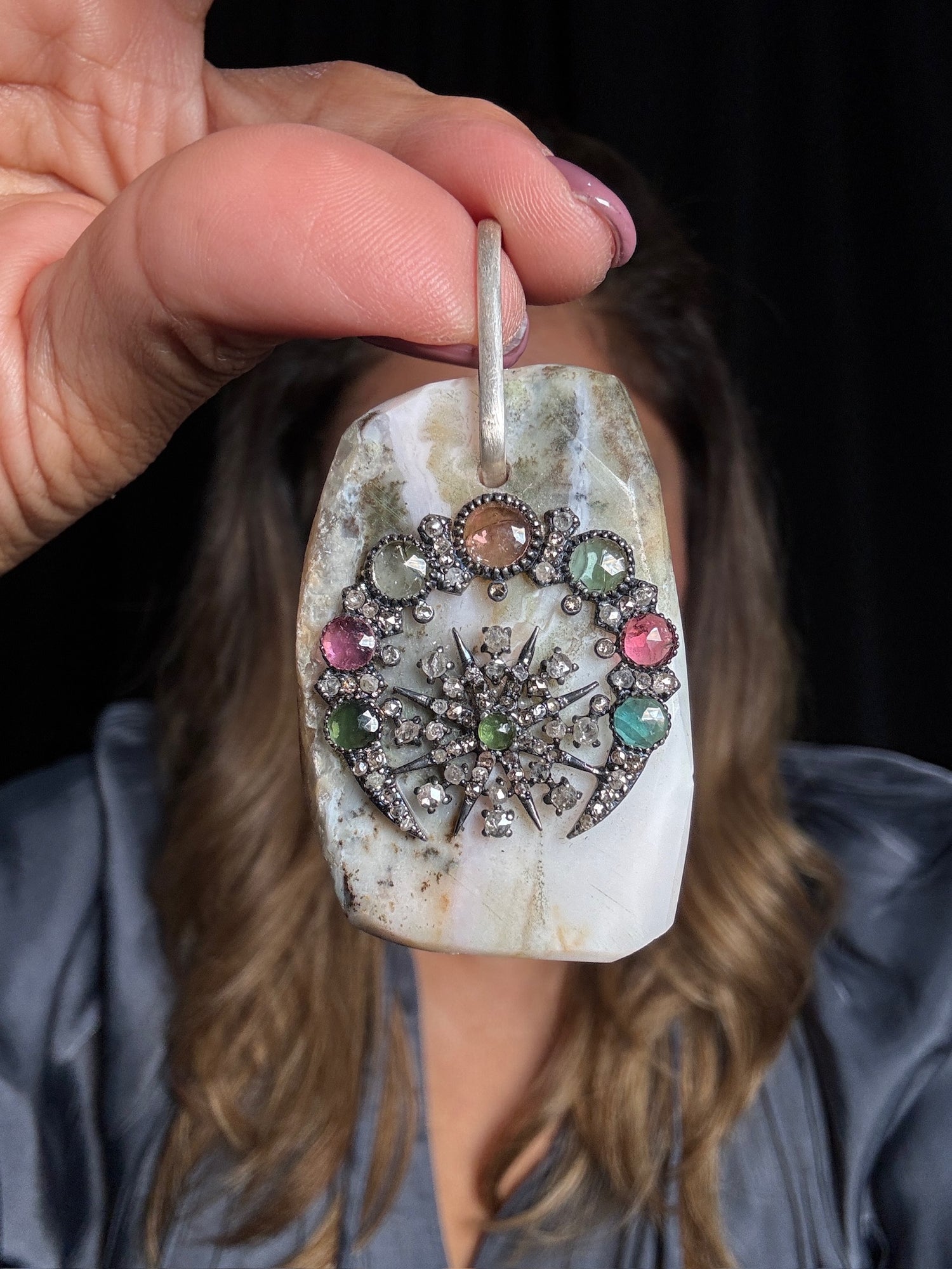 Hand-held pink opal pendant with ornate sterling silver diamond-encrusted starburst design featuring multicolored tourmaline gemstones in pink, green, and blue hues
