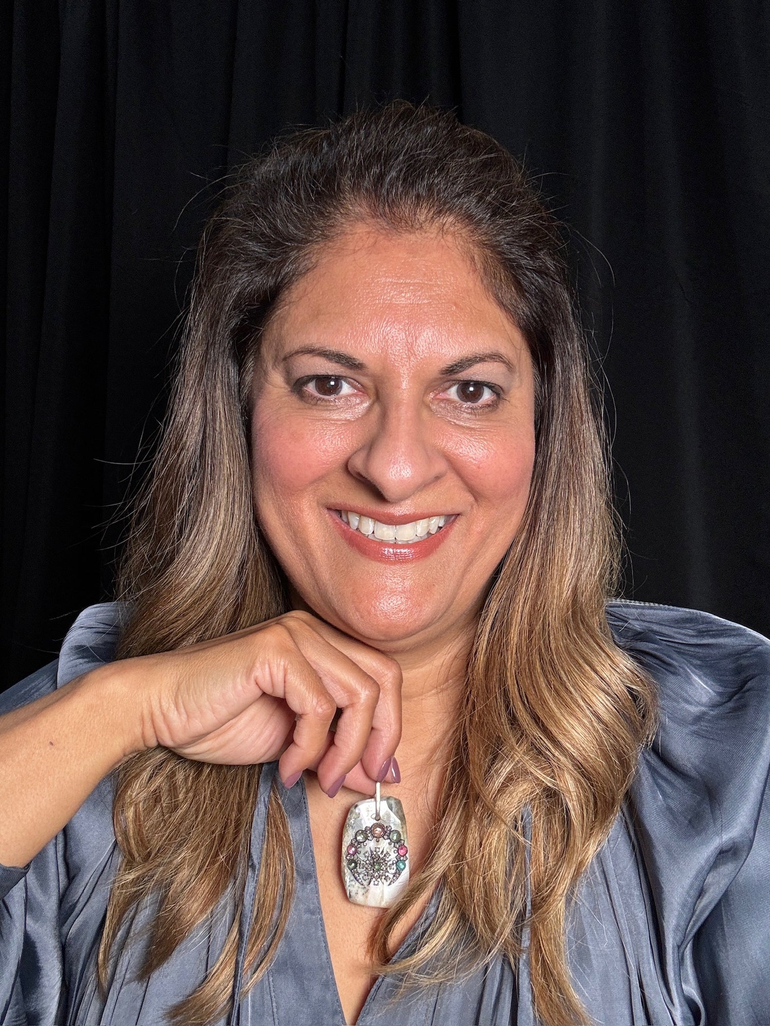 Smiling woman wearing blue shirt displays pink opal pendant with colorful tourmaline gems and diamond accents in sterling silver setting