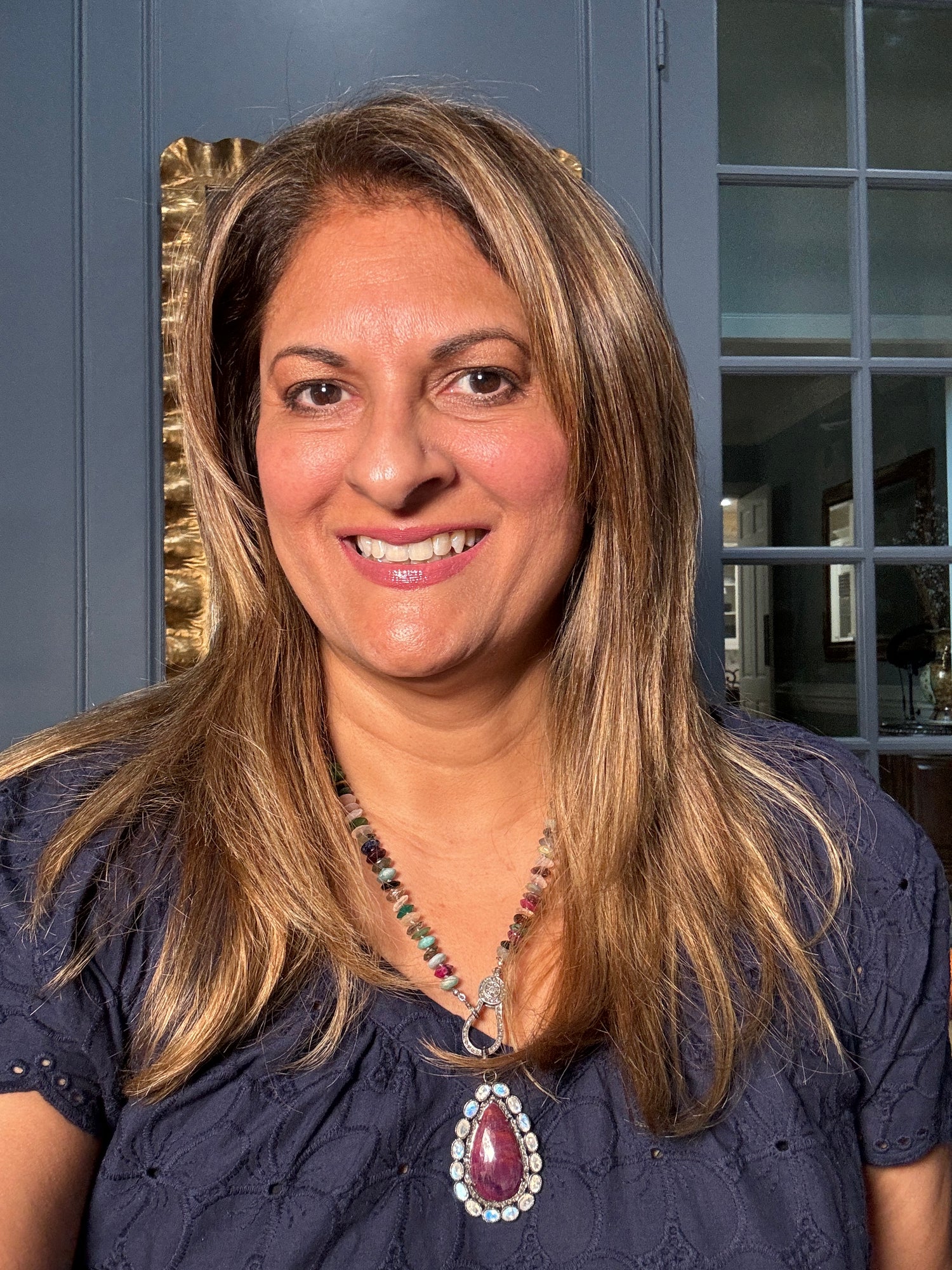 Woman wearing vibrant mixed gemstone necklace with large ruby moonstone teardrop pendant surrounded by diamonds, showcasing the 22-inch length and rainbow-colored beaded design
