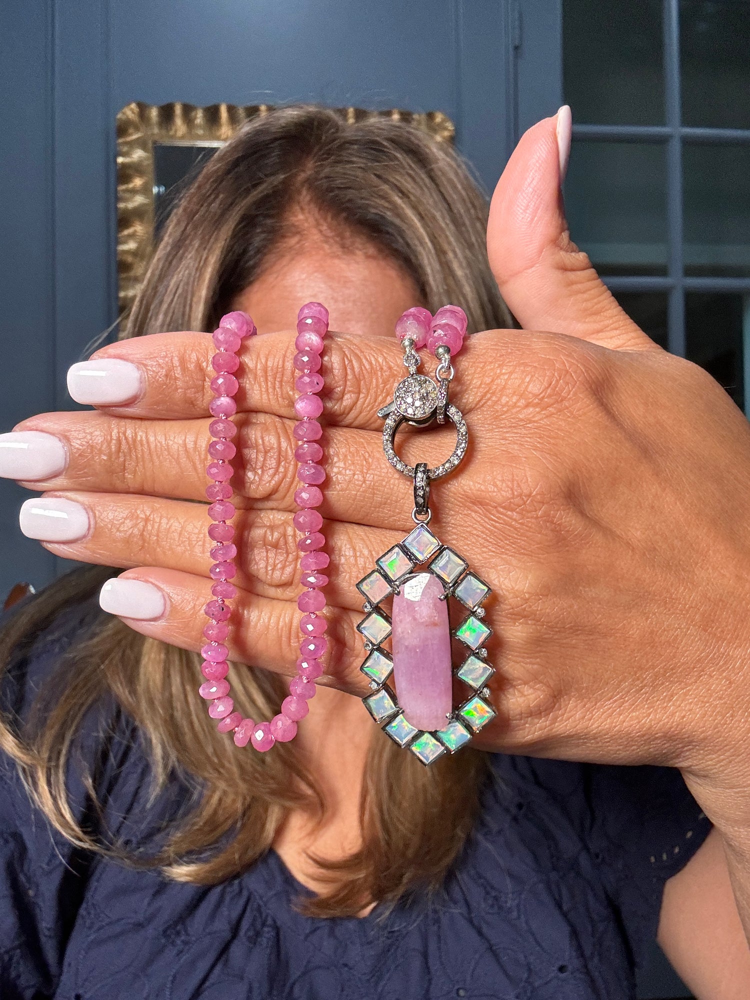 Woman holding pink sapphire beaded necklace with ornate opal and diamond pendant featuring rectangular pink sapphire center stone surrounded by opals in sterling silver