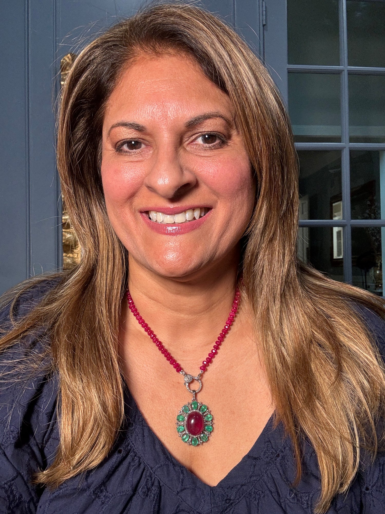 Woman wearing 18-inch ruby necklace with emerald and diamond halo pendant against navy top, showcasing the luxurious gemstone combination