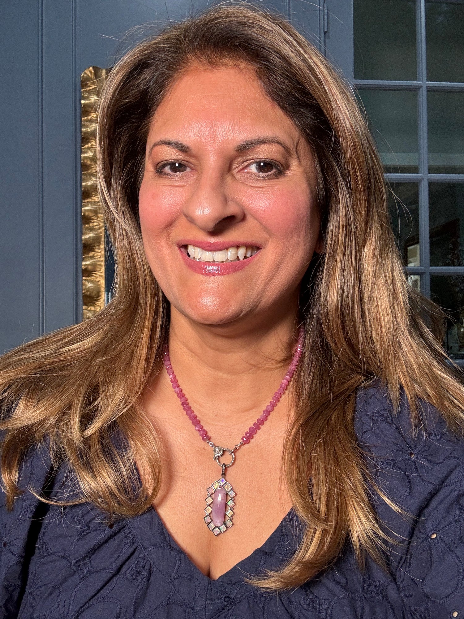 Woman wearing 19-inch pink sapphire bead necklace with geometric opal and pink sapphire pendant, modeled against blue door background
