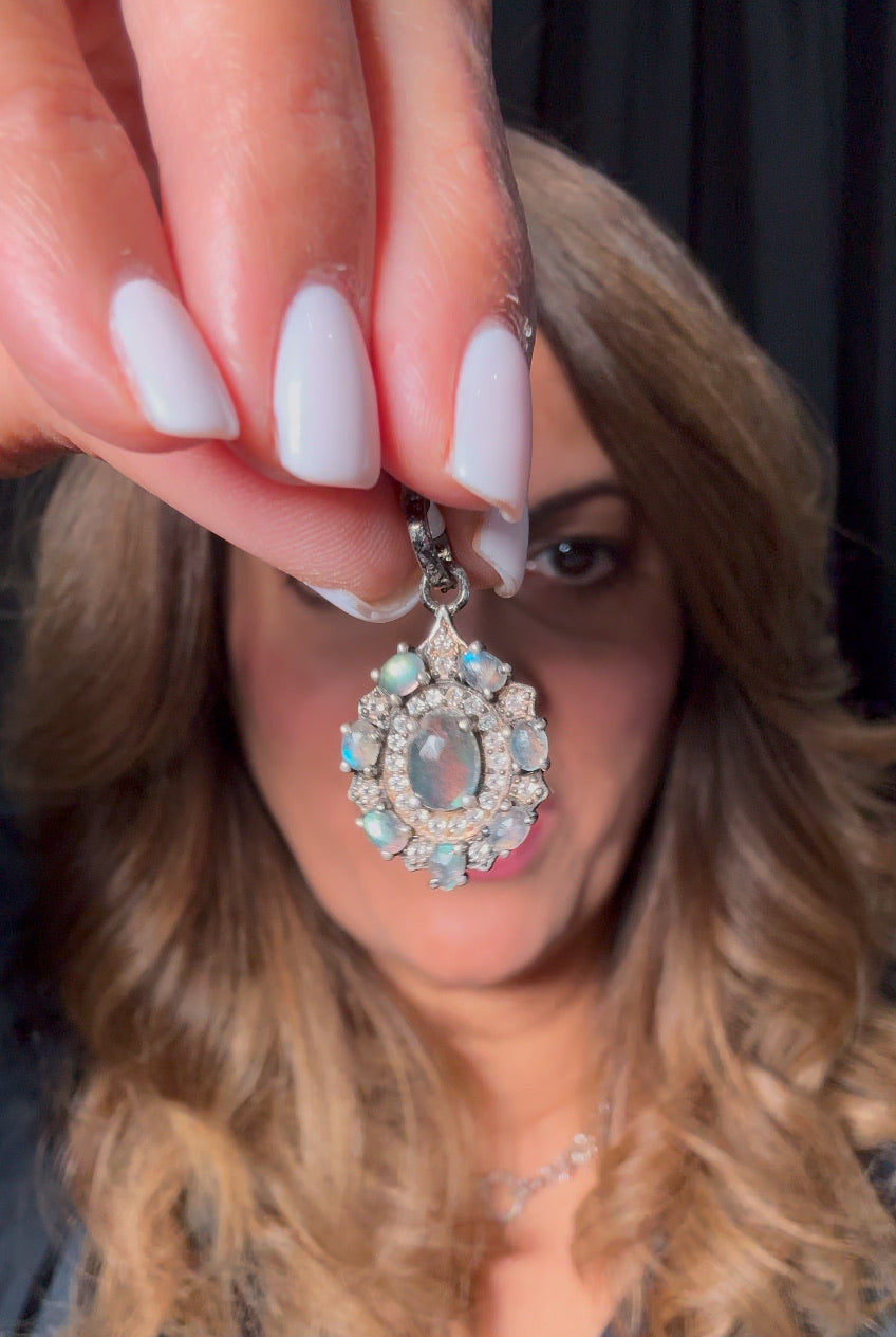 Hand-held ornate sterling silver pendant featuring central gray labradorite surrounded by smaller blue labradorite stones and sparkling diamonds in decorative setting