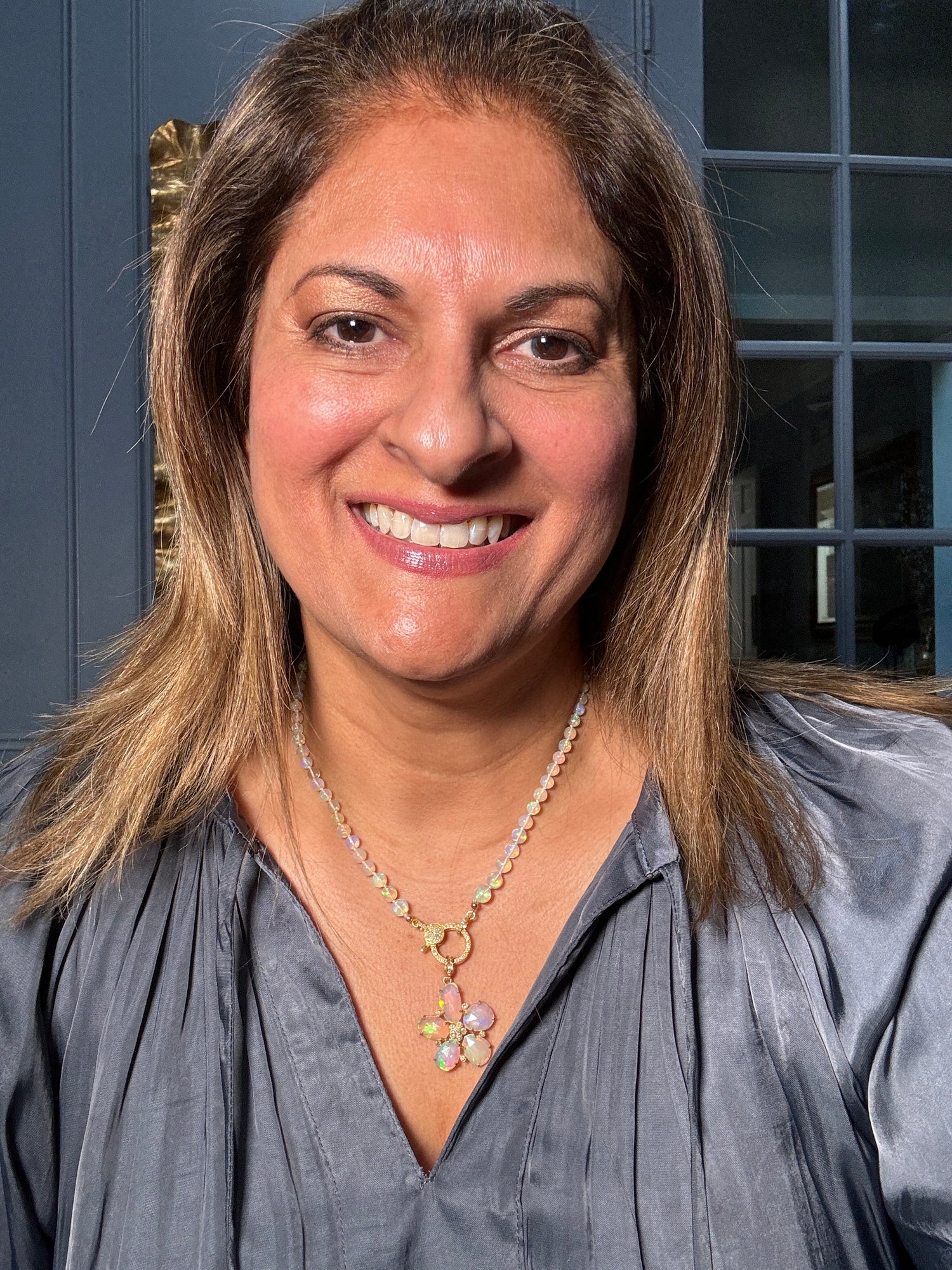 Woman wearing 18-inch Ethiopian opal beaded necklace with gold floral pendant, showing how the iridescent stones catch light beautifully