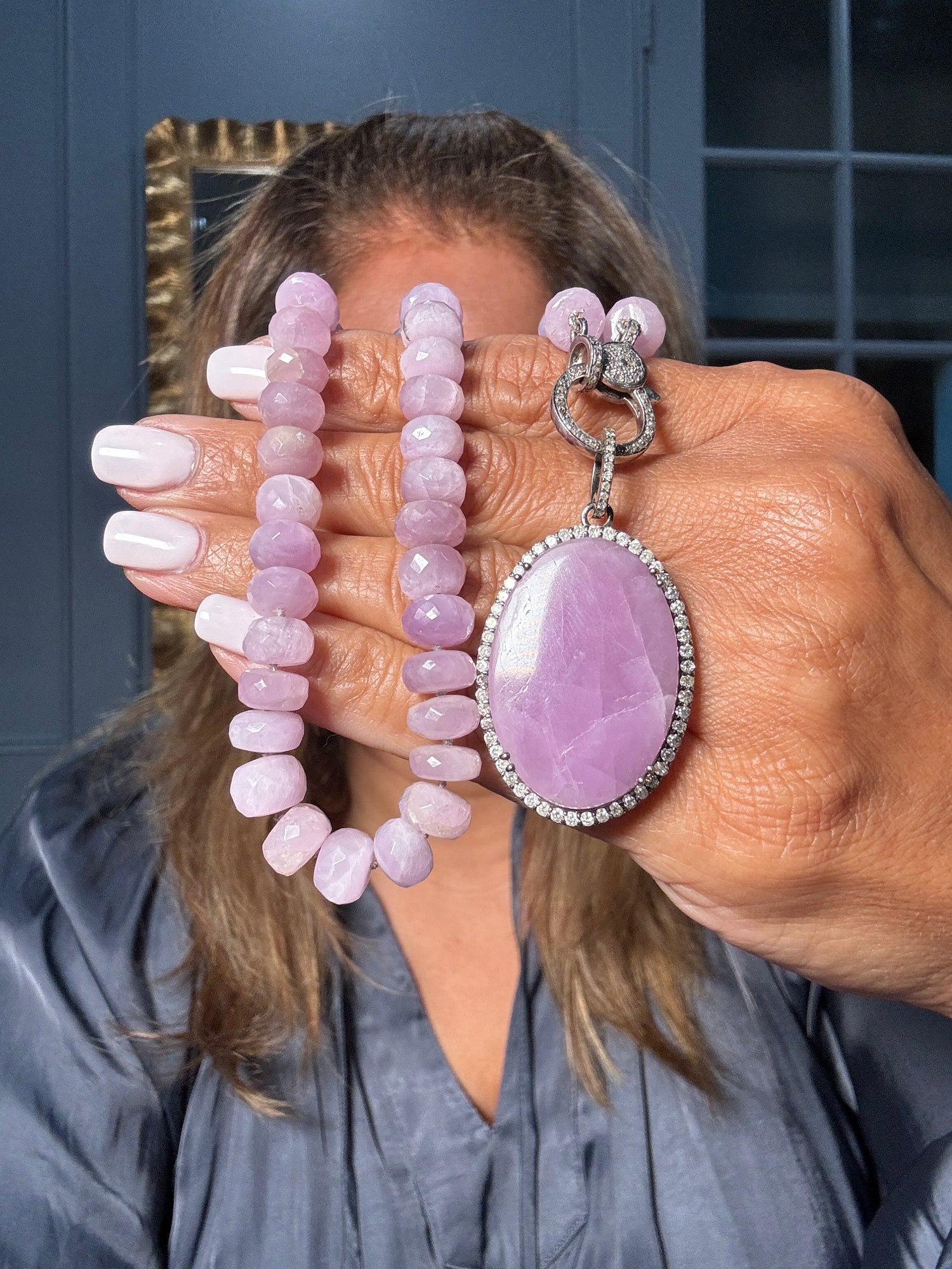 Hand holding lilac pink kunzite beaded necklace with large oval kunzite and diamond pendant in sterling silver setting