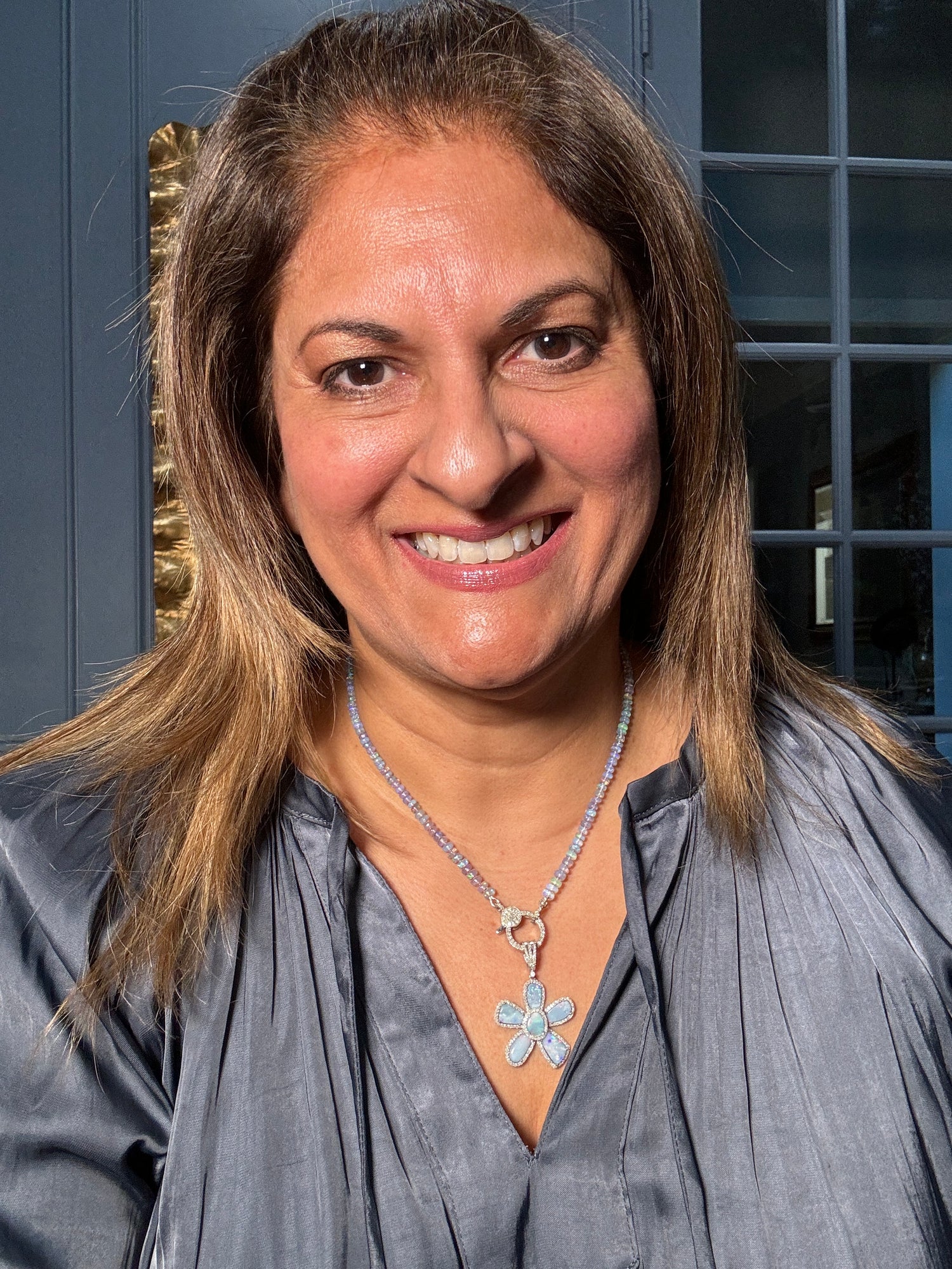 Woman wearing 18-inch Ethiopian opal necklace with cool-toned blue and purple opal flower pendant, styled with gray silk blouse for elegant dinner look