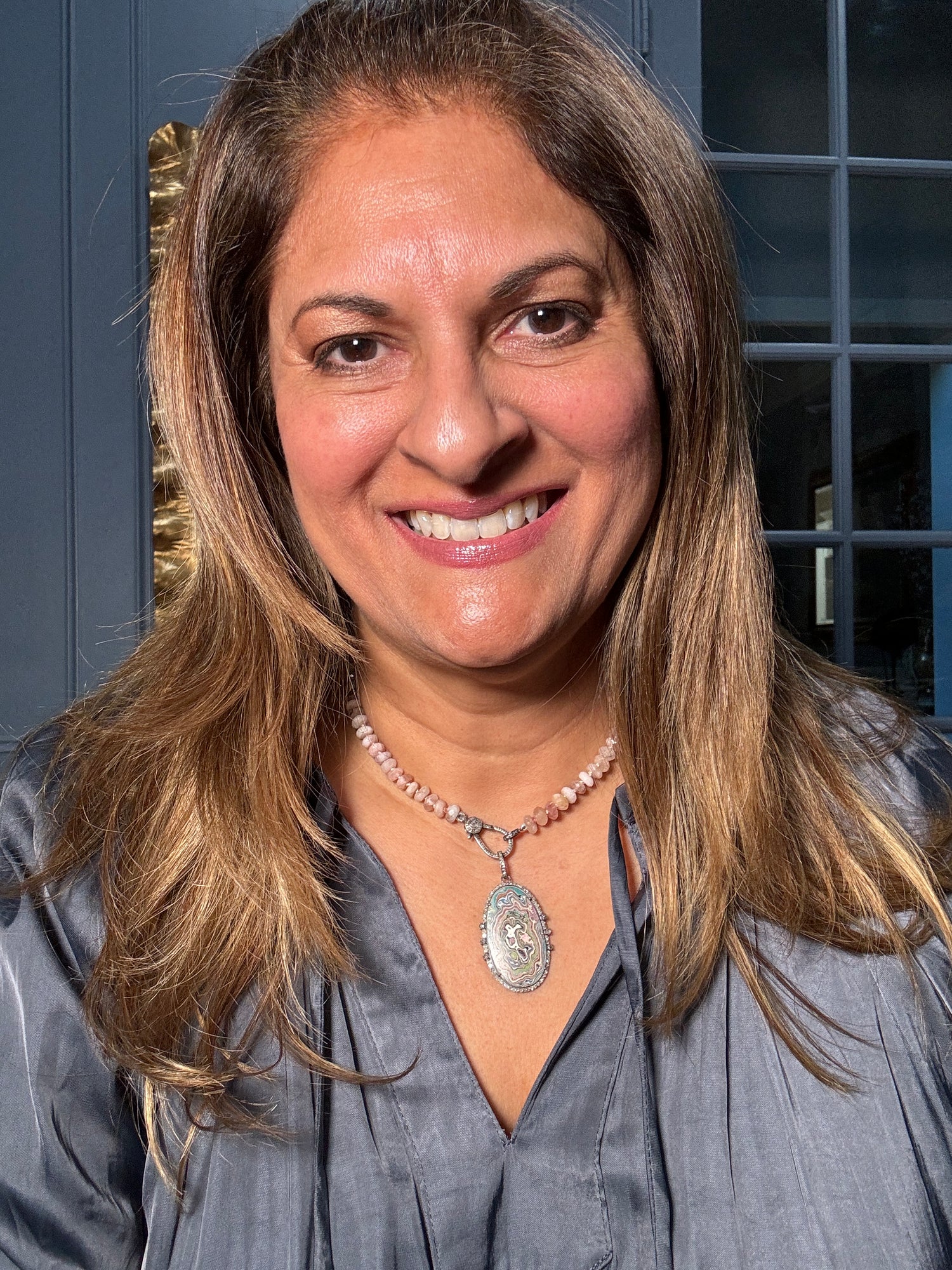 Woman wearing morganite necklace with vintage fordite pendant featuring pastel swirled patterns against gray shirt, smiling at camera