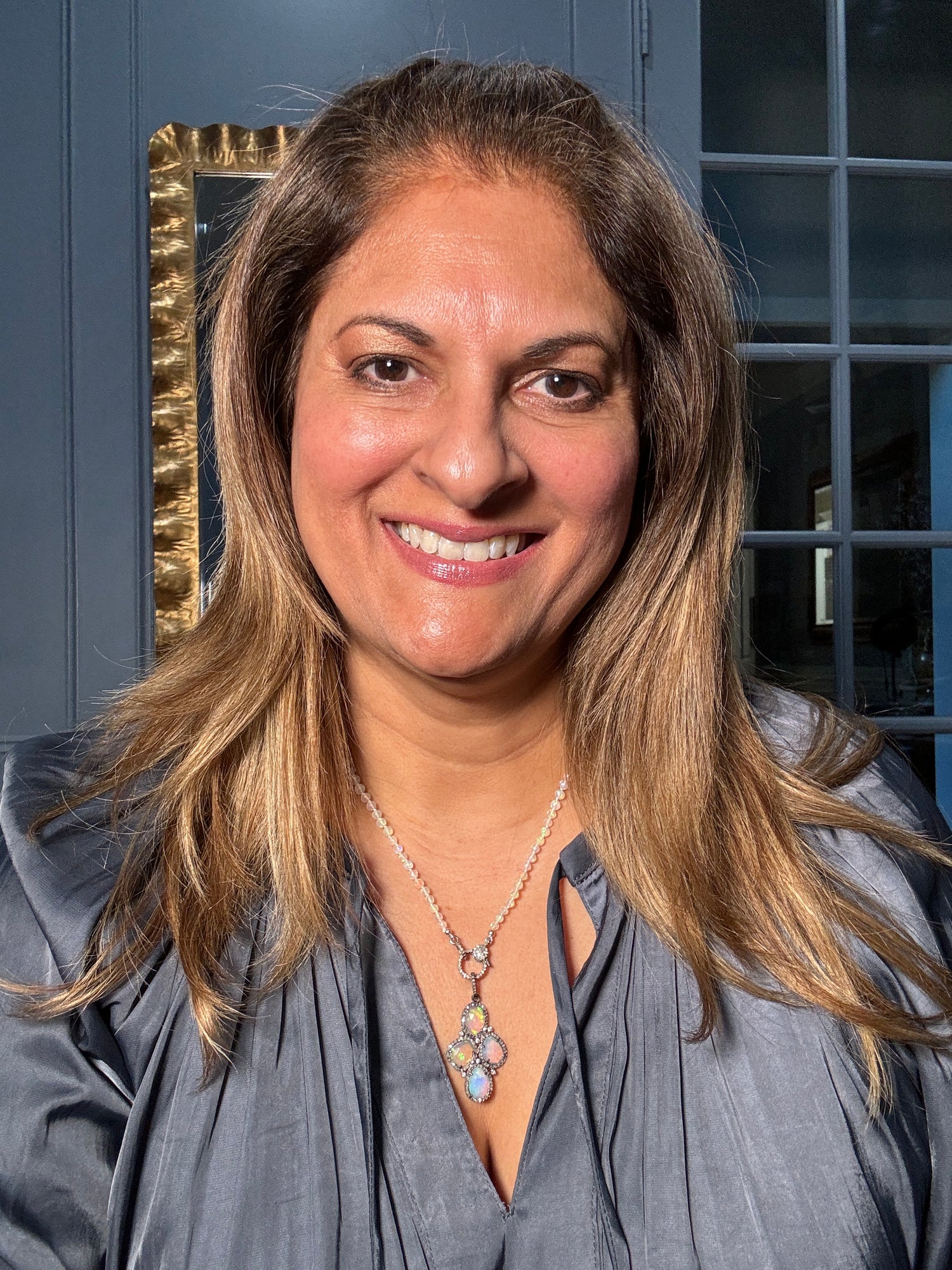 Woman wearing 20-inch Ethiopian opal necklace with multi-stone pendant, showcasing iridescent blue and green opal beads with diamond clasp against gray blouse