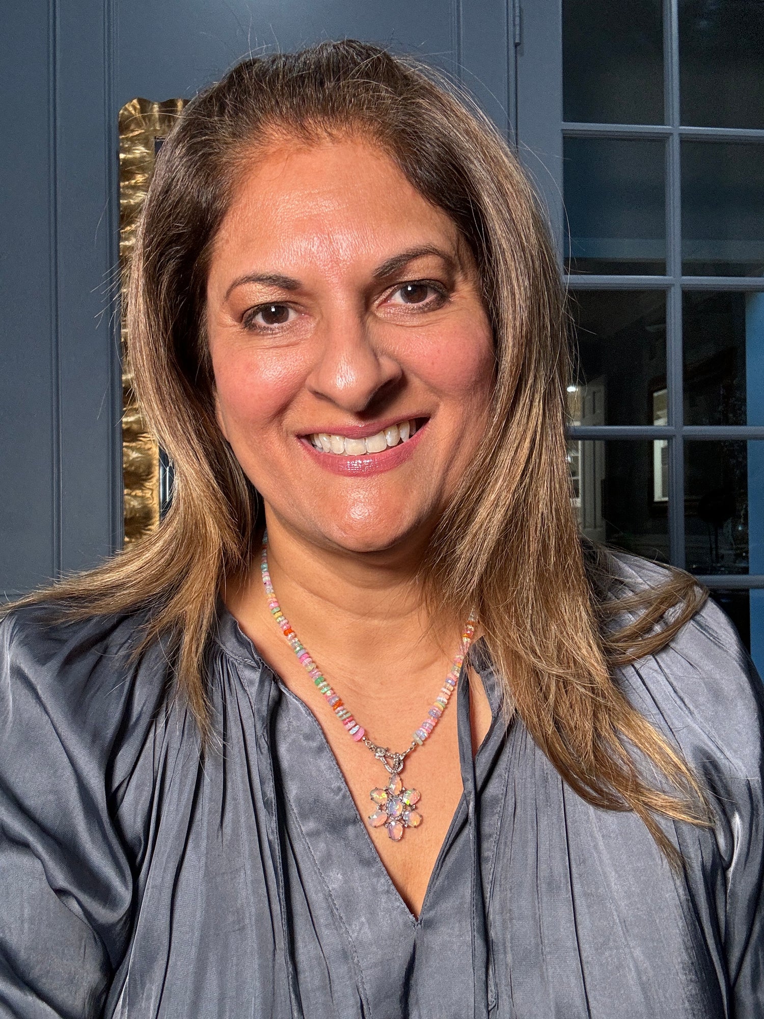 Woman wearing 19-inch Ethiopian opal beaded necklace with ornate sterling silver and diamond flower pendant, showcasing colorful fire opals against gray blouse