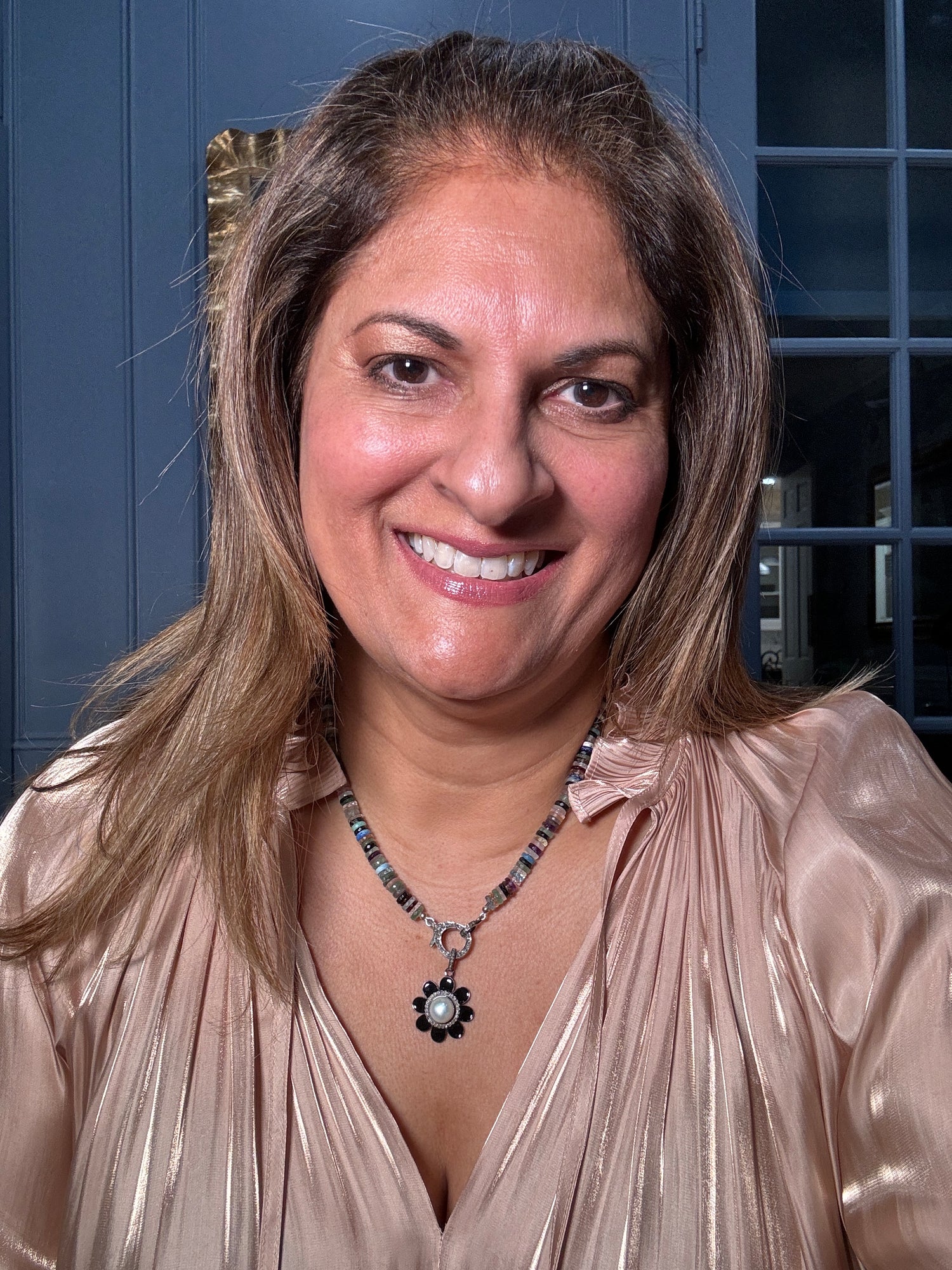 Smiling woman wearing an 18-inch mixed gemstone necklace with tourmaline, amethyst, and fluorite beads, showcasing the black onyx flower pendant with pearl center against champagne blouse