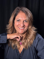 Smiling blonde woman wearing statement oval ruby pendant with diamond halo on sterling silver chain, photographed against black backdrop