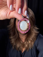 Hand holding an elegant moonstone and ruby pendant with pink gemstones surrounding a luminous white center stone in sterling silver setting